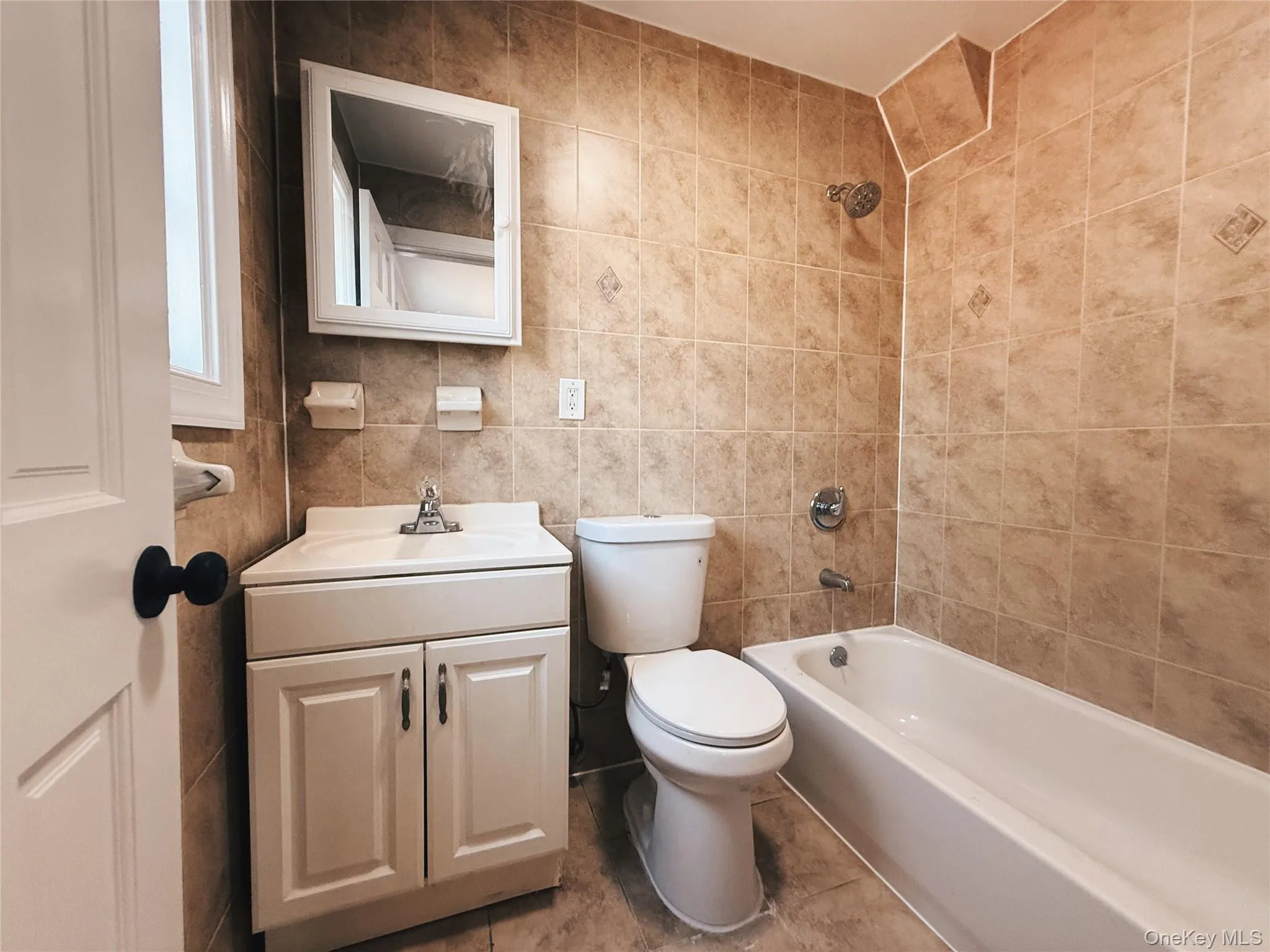 Private bathroom featuring full-height tiled walls, white vanity with integrated sink, white medicine cabinet, and a shower-over-tub combination with chrome fixtures. Private bathroom featuring full-height tiled walls, white vanity with integrated sink, white medicine cabinet, and a shower-over-tub combination with chrome fixtures.