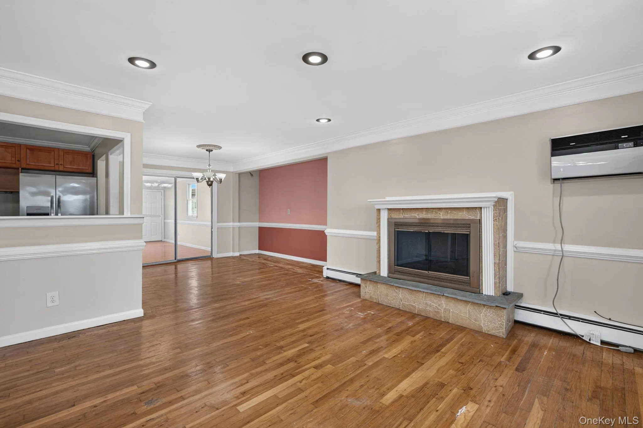 Living area featuring wood-finish flooring, a fireplace with a stone surround and hearth, recessed lighting, and crown molding Living area featuring wood-finish flooring, a fireplace with a stone surround and hearth, recessed lighting, and crown molding
