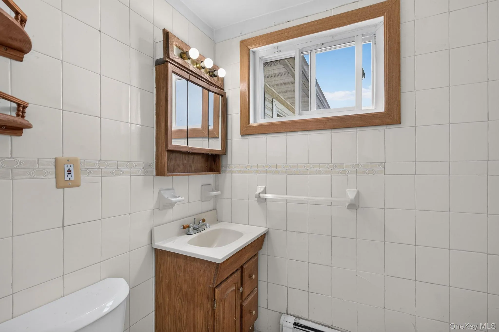 Bathroom featuring white square wall tiles with a decorative border, a wood-finish vanity with an integrated sink, and a matching wood-finish medicine cabinet with task lighting Bathroom featuring white square wall tiles with a decorative border, a wood-finish vanity with an integrated sink, and a matching wood-finish medicine cabinet with task lighting