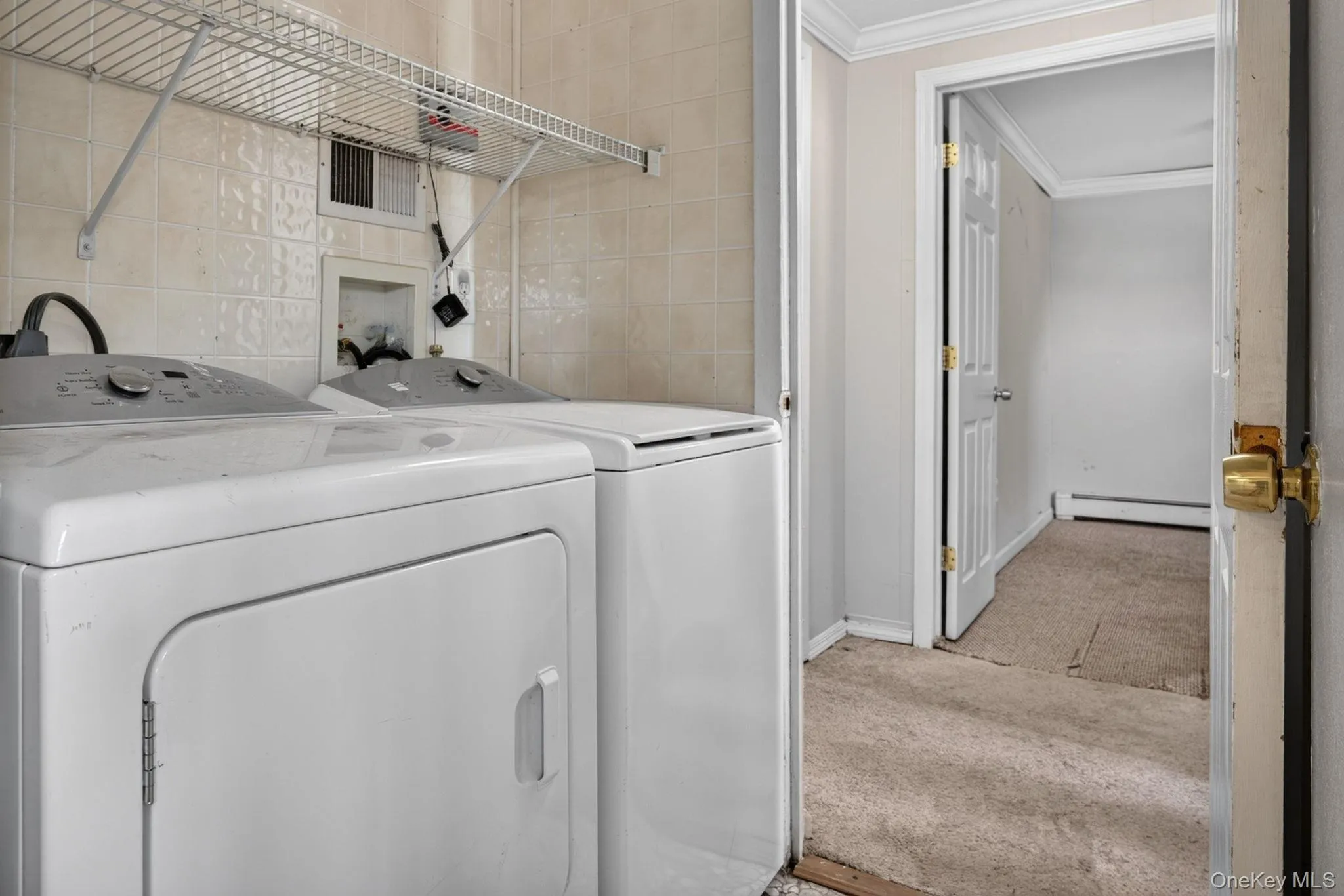 Dedicated laundry area featuring a washer and dryer set, tiled wall, and wire shelving Dedicated laundry area featuring a washer and dryer set, tiled wall, and wire shelving