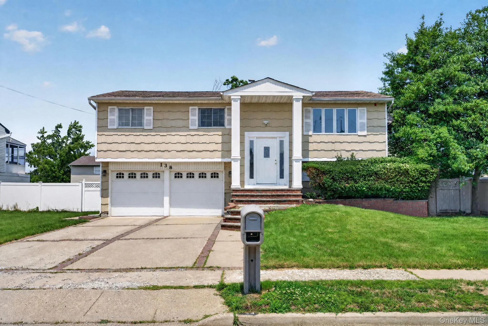 Split-level residence featuring a two-car garage, concrete driveway with brick accents, and a covered front entry with white columns Split-level residence featuring a two-car garage, concrete driveway with brick accents, and a covered front entry with white columns