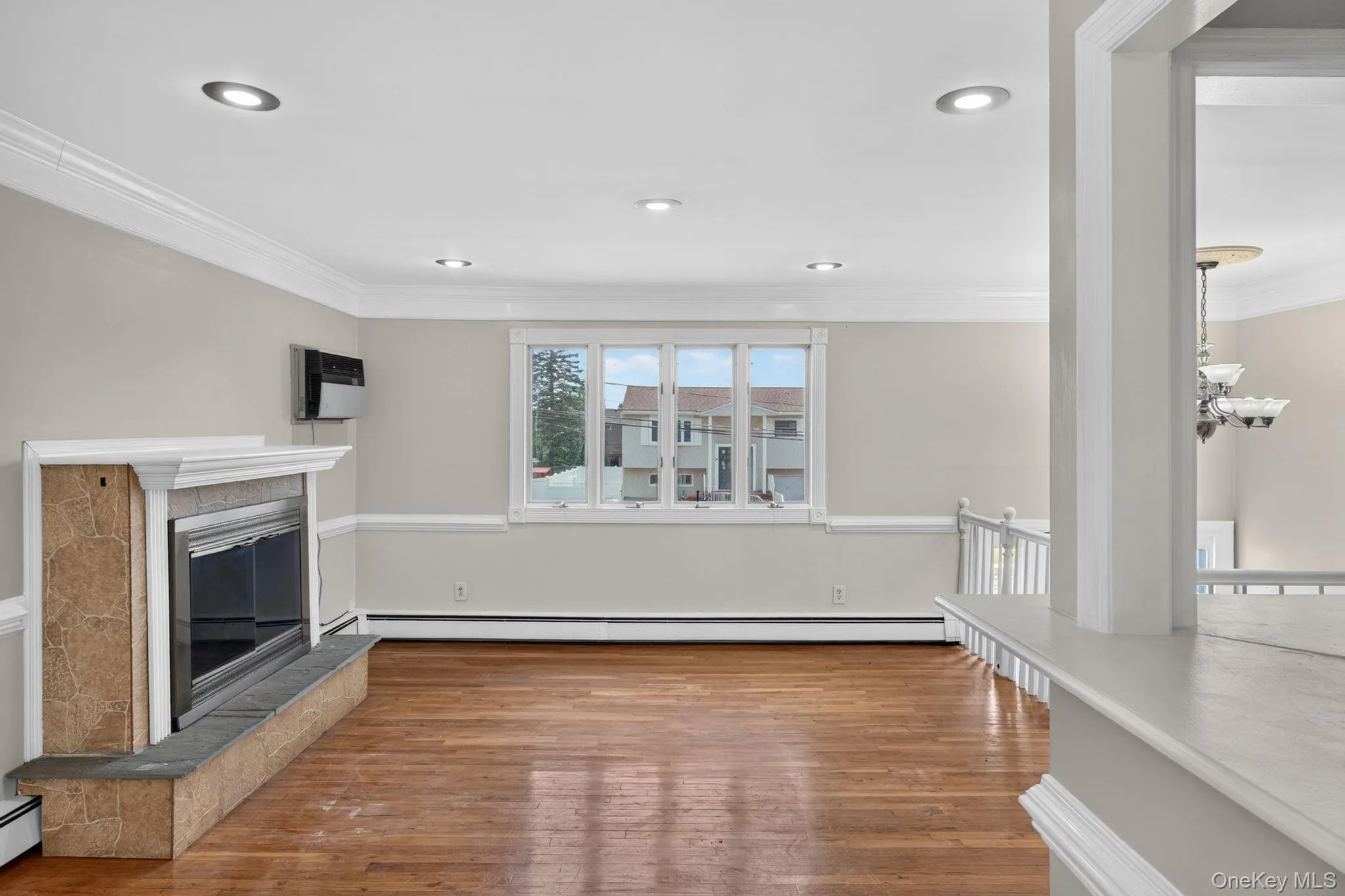 Living area featuring hardwood flooring, a fireplace with a stone surround and hearth, recessed lighting, crown molding, and a multi-pane window Living area featuring hardwood flooring, a fireplace with a stone surround and hearth, recessed lighting, crown molding, and a multi-pane window