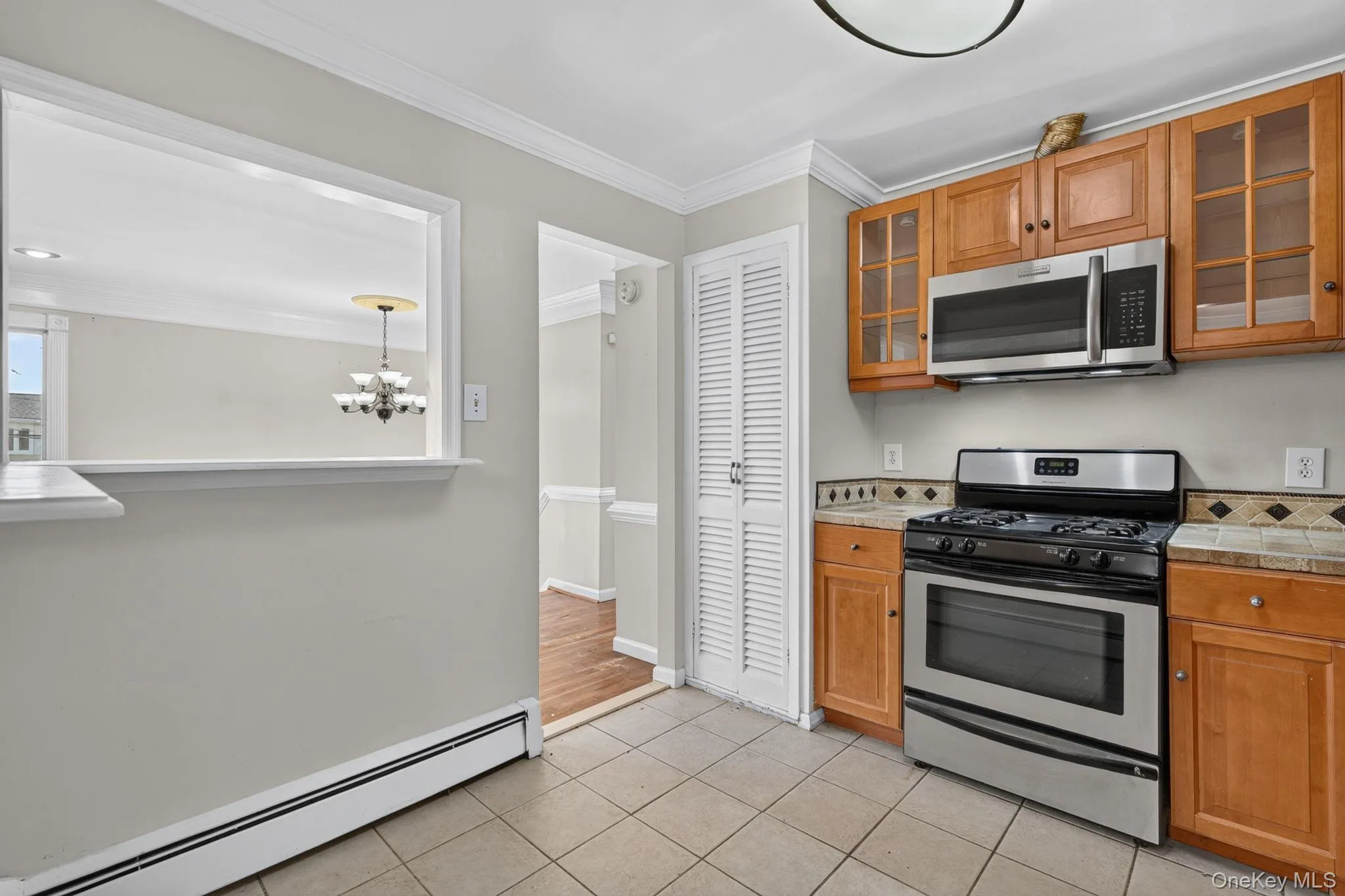 Kitchen featuring light wood cabinetry, stainless steel range and microwave, tiled countertops with decorative backsplash, and tiled flooring Kitchen featuring light wood cabinetry, stainless steel range and microwave, tiled countertops with decorative backsplash, and tiled flooring