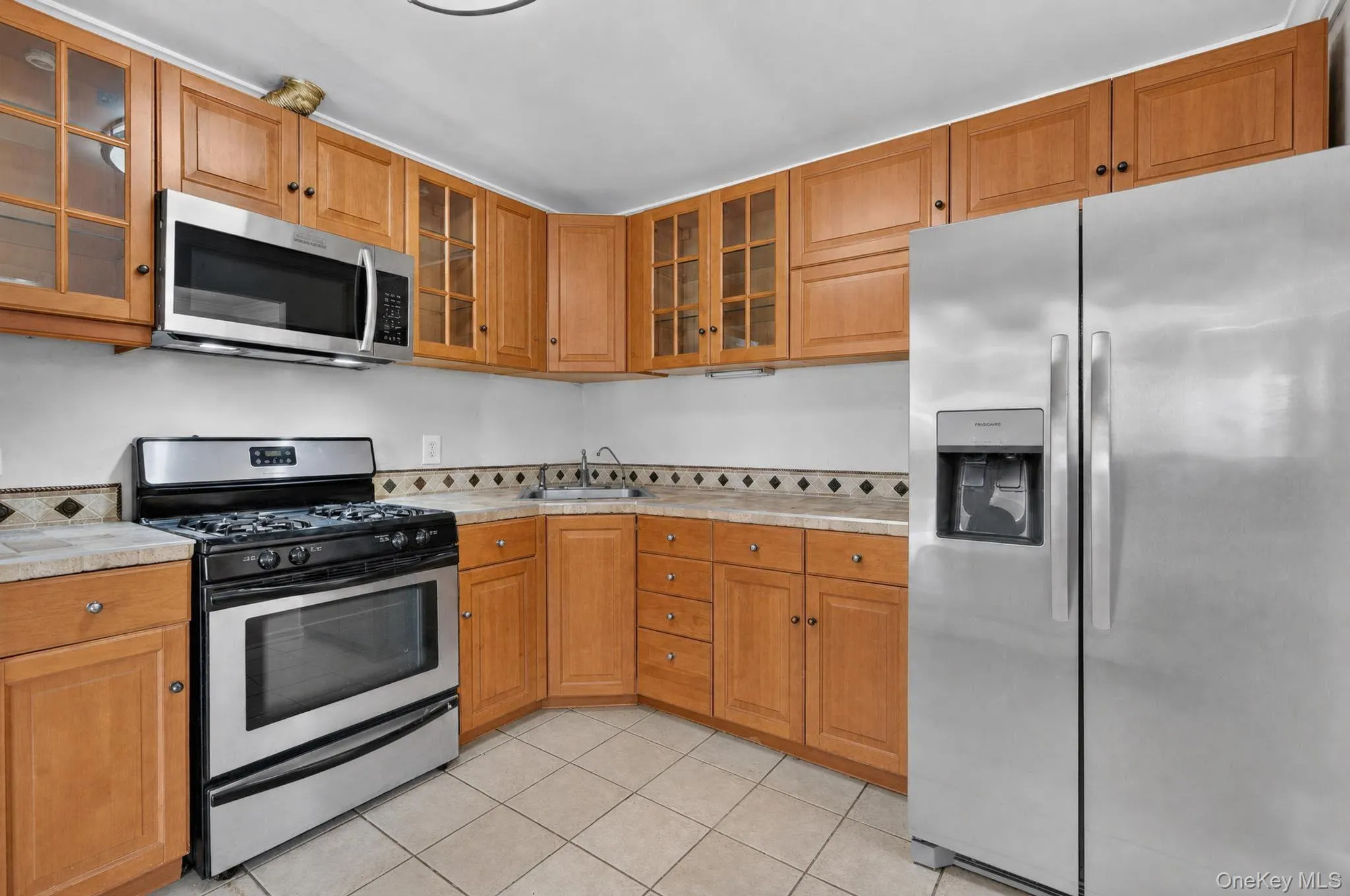 Kitchen featuring stainless steel appliances, light wood cabinetry, and a patterned tile backsplash Kitchen featuring stainless steel appliances, light wood cabinetry, and a patterned tile backsplash