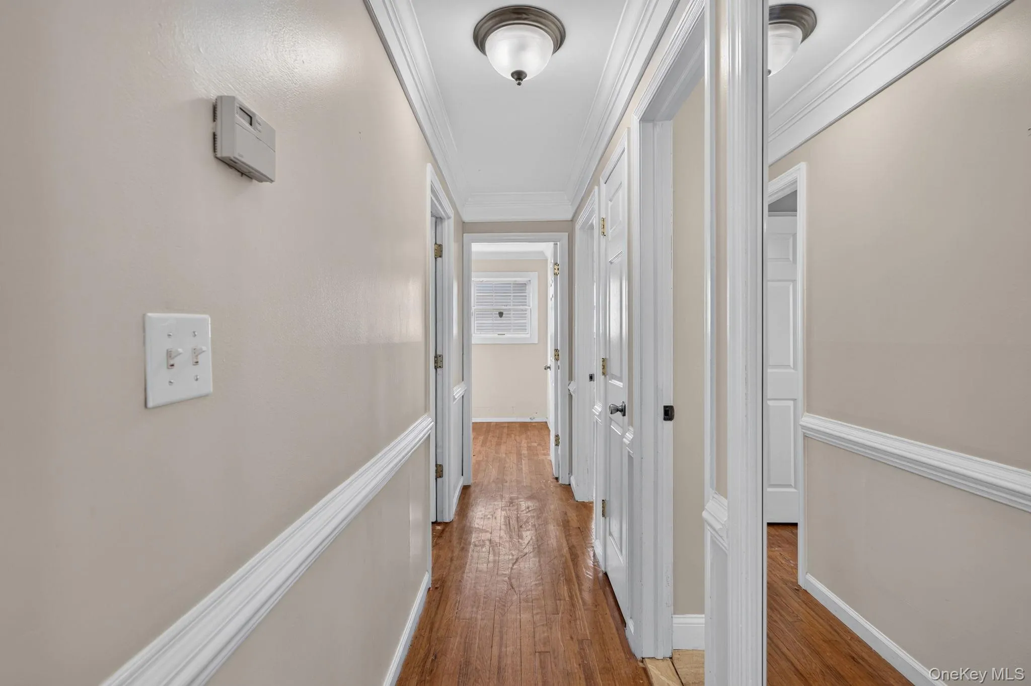 Hallway featuring wood-finish flooring, light-toned walls with chair rail molding, and white trim Hallway featuring wood-finish flooring, light-toned walls with chair rail molding, and white trim