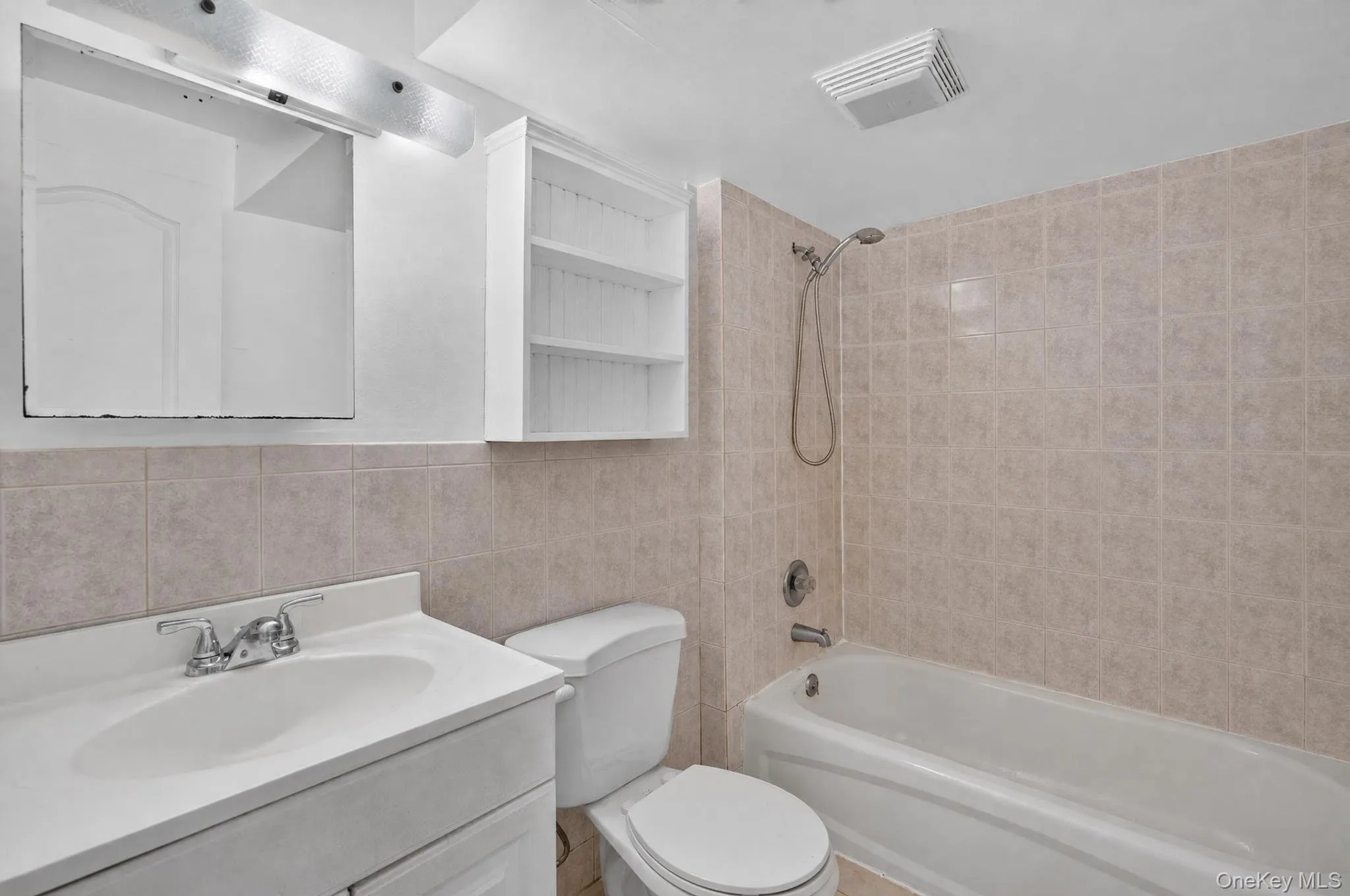 Full bathroom featuring a single vanity, a toilet, a tub with a shower head, and tiled walls Full bathroom featuring a single vanity, a toilet, a tub with a shower head, and tiled walls