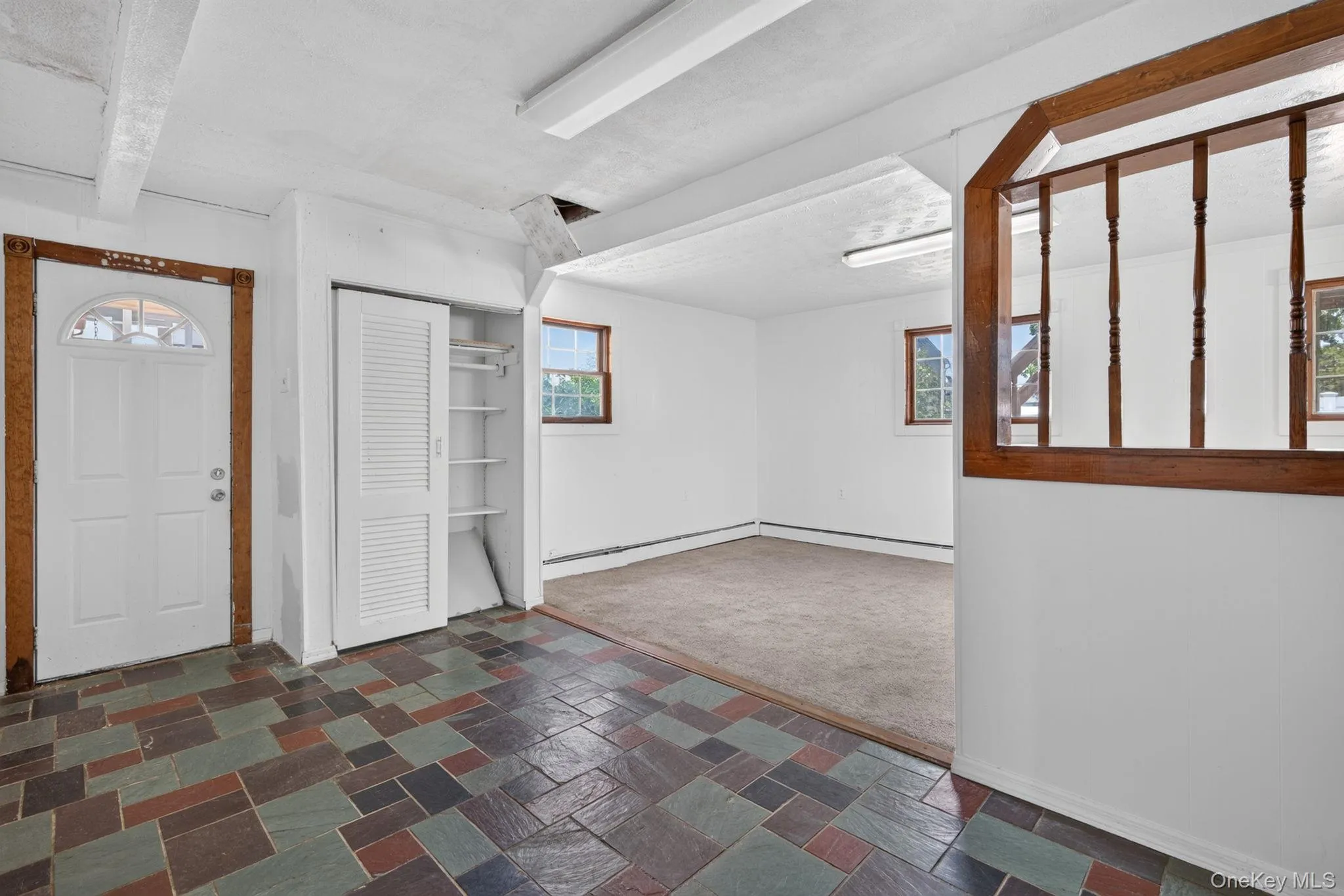Multi-color slate tile flooring at entry, featuring a white door with an arched window, and a built-in closet with louvered bi-fold doors and shelving Multi-color slate tile flooring at entry, featuring a white door with an arched window, and a built-in closet with louvered bi-fold doors and shelving