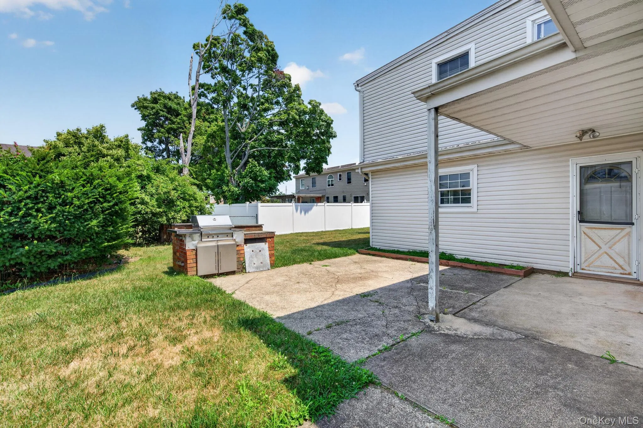 Rear exterior featuring a covered patio area with a concrete surface, white vinyl siding, a built-in brick barbecue station, and a fenced yard Rear exterior featuring a covered patio area with a concrete surface, white vinyl siding, a built-in brick barbecue station, and a fenced yard