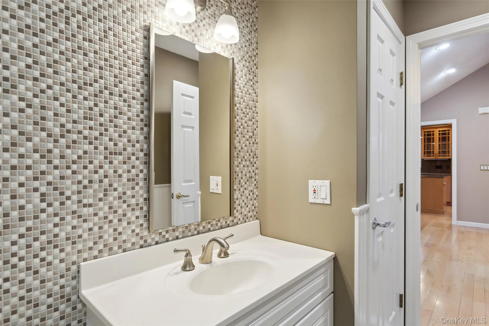 Bathroom featuring vaulted ceiling, wood finished floors, vanity, baseboards, and an accent wall Bathroom featuring vaulted ceiling, wood finished floors, vanity, baseboards, and an accent wall