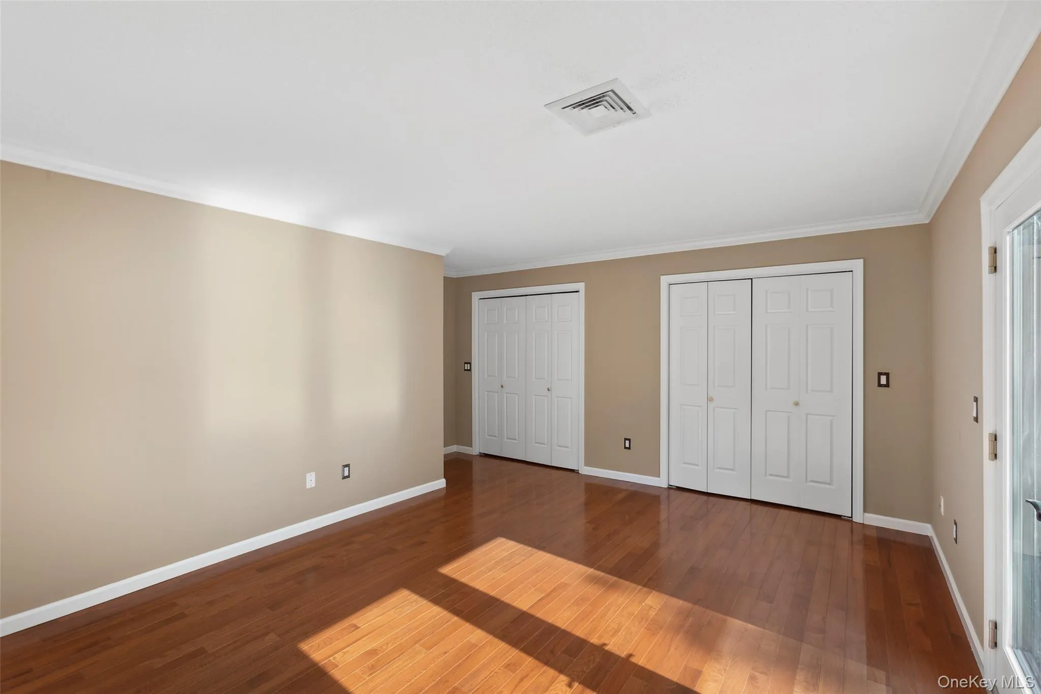 Unfurnished bedroom with baseboards, two closets, wood finished floors, and visible vents Unfurnished bedroom with baseboards, two closets, wood finished floors, and visible vents