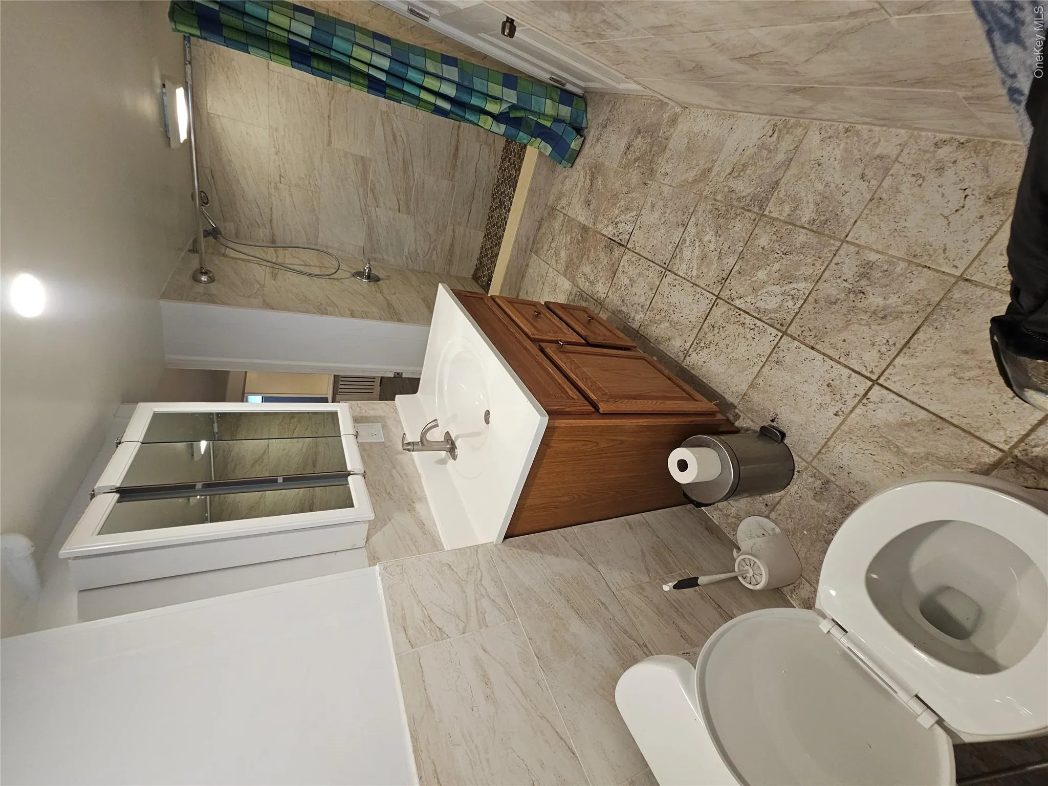 Bathroom featuring a single vanity with a white countertop and wood-finish cabinetry Bathroom featuring a single vanity with a white countertop and wood-finish cabinetry