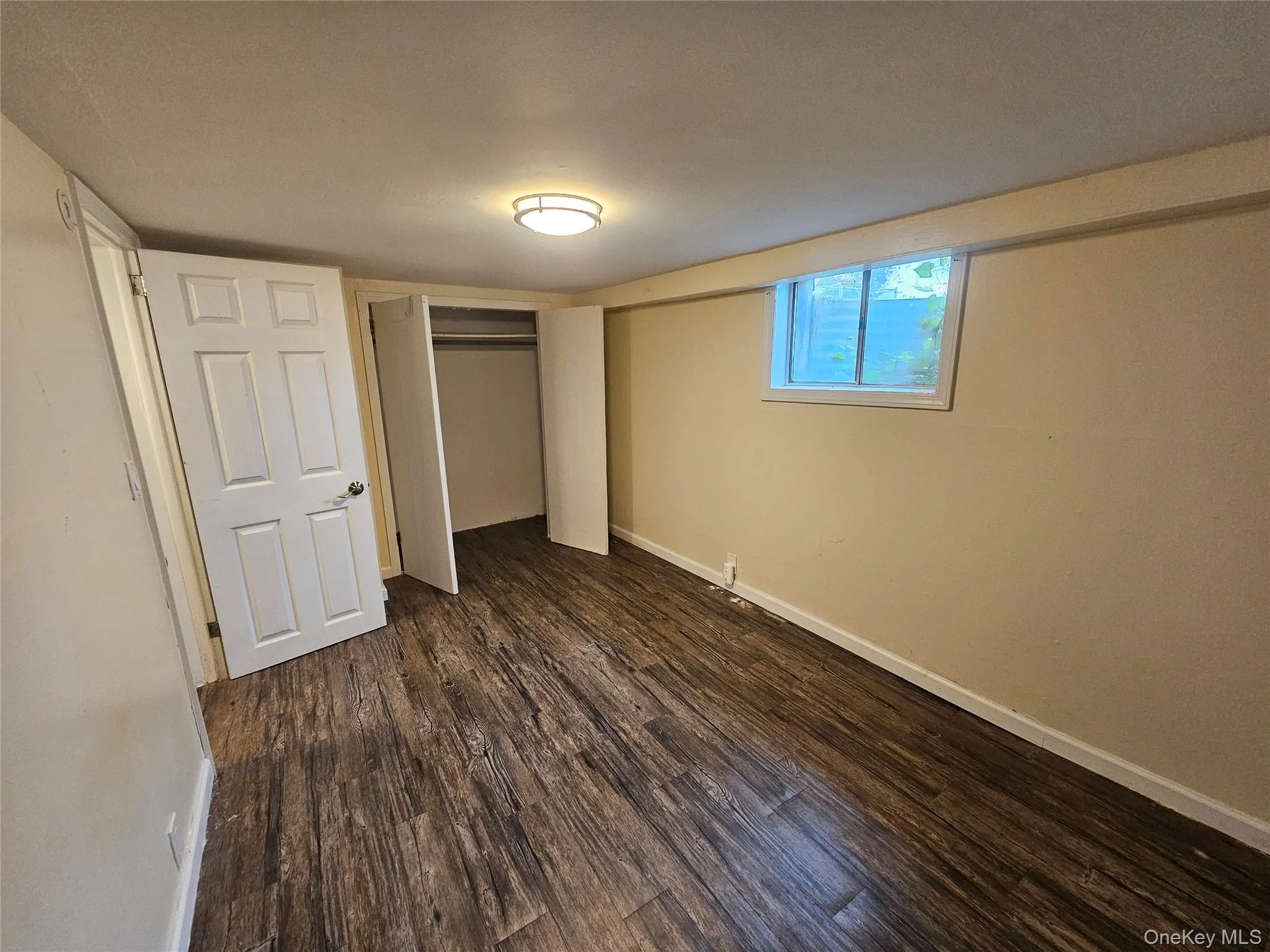Interior room featuring wood-finish flooring, a flush-mount ceiling light fixture, and a window with white trim Interior room featuring wood-finish flooring, a flush-mount ceiling light fixture, and a window with white trim