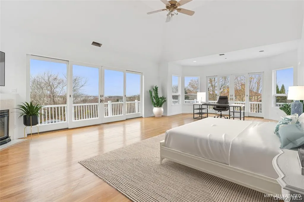 Expansive bedroom featuring vaulted ceilings, wood-finish flooring, a fireplace with a stone surround, and multiple floor-to-ceiling windows with balcony access Expansive bedroom featuring vaulted ceilings, wood-finish flooring, a fireplace with a stone surround, and multiple floor-to-ceiling windows with balcony access
