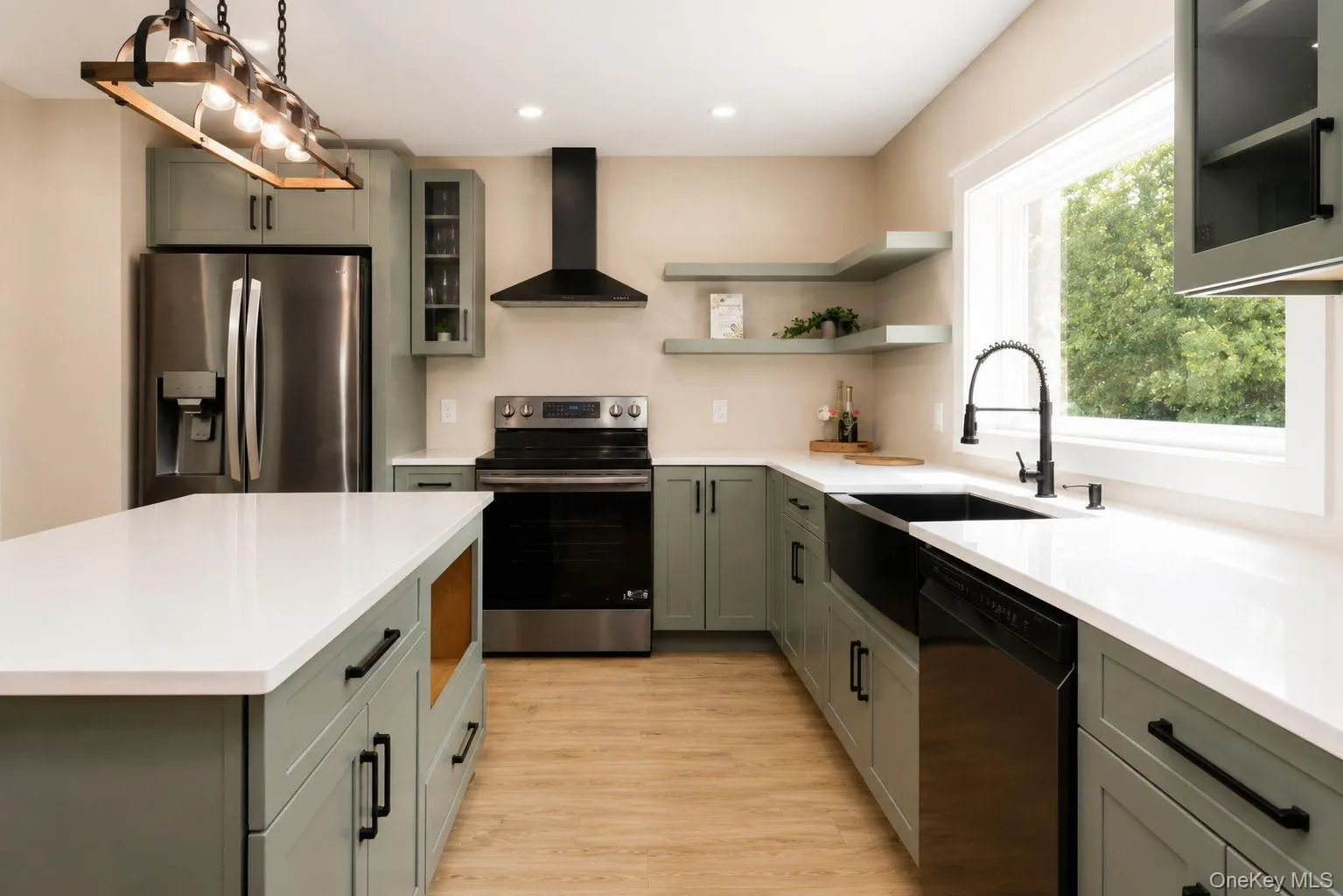 Modern kitchen featuring light green cabinetry, white countertops, stainless steel appliances, a black farmhouse sink with a black gooseneck faucet, and wood-finish flooring Modern kitchen featuring light green cabinetry, white countertops, stainless steel appliances, a black farmhouse sink with a black gooseneck faucet, and wood-finish flooring