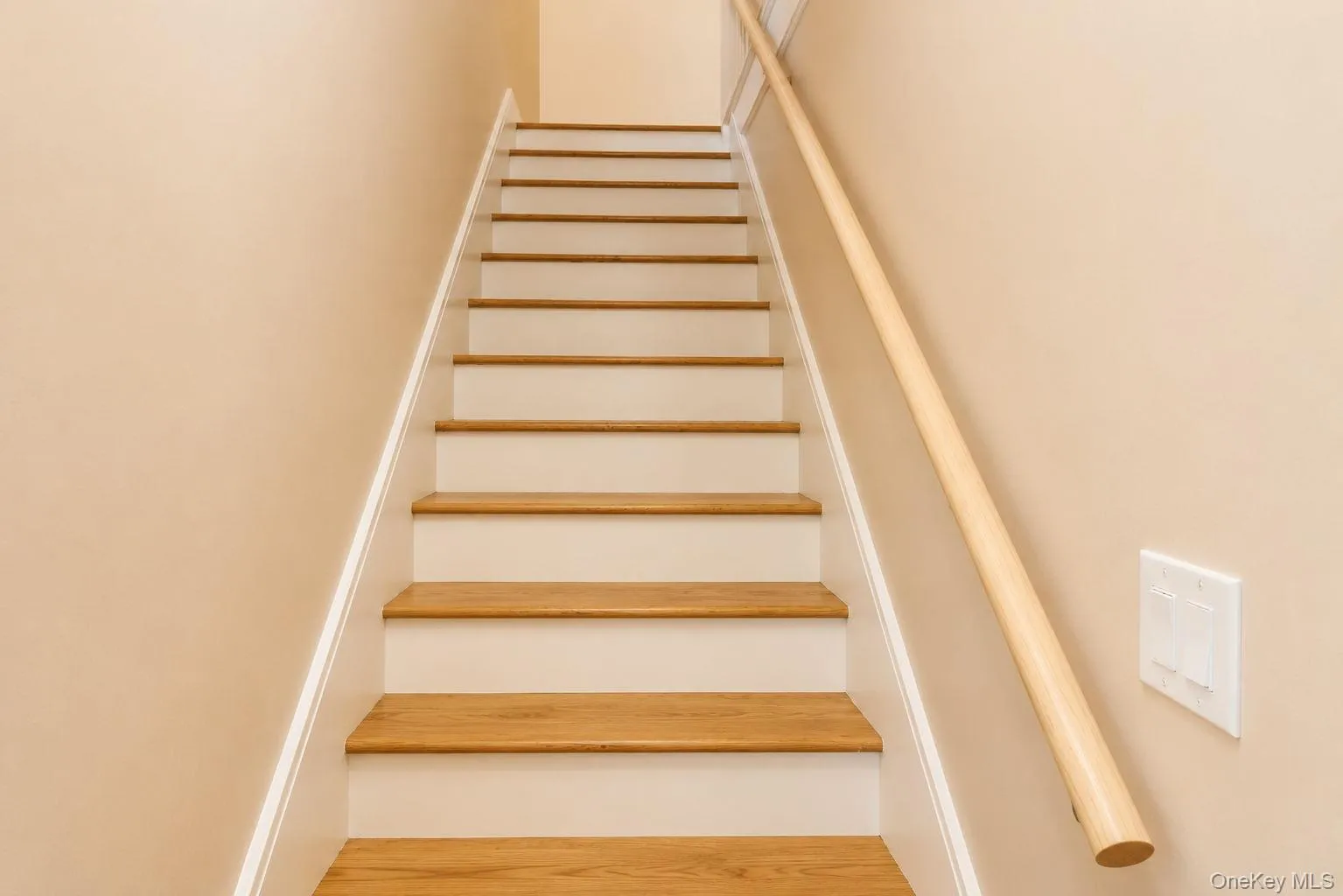 Staircase featuring wood-finish treads, white risers, a light wood-finish handrail, and a neutral wall color Staircase featuring wood-finish treads, white risers, a light wood-finish handrail, and a neutral wall color