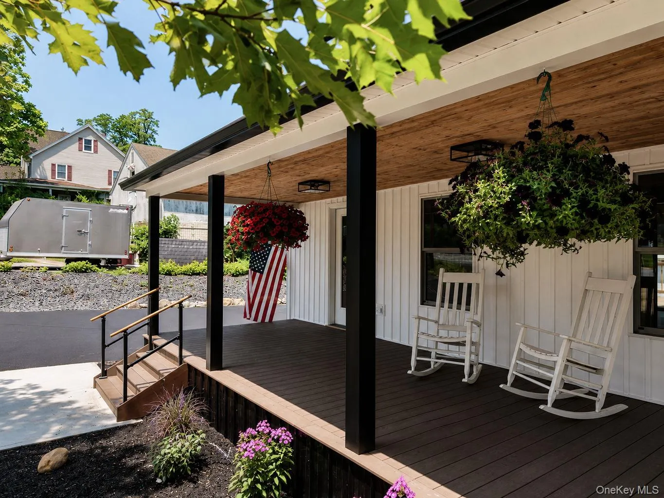 Covered front porch featuring a wood-finish ceiling, dark composite decking, and black support columns Covered front porch featuring a wood-finish ceiling, dark composite decking, and black support columns