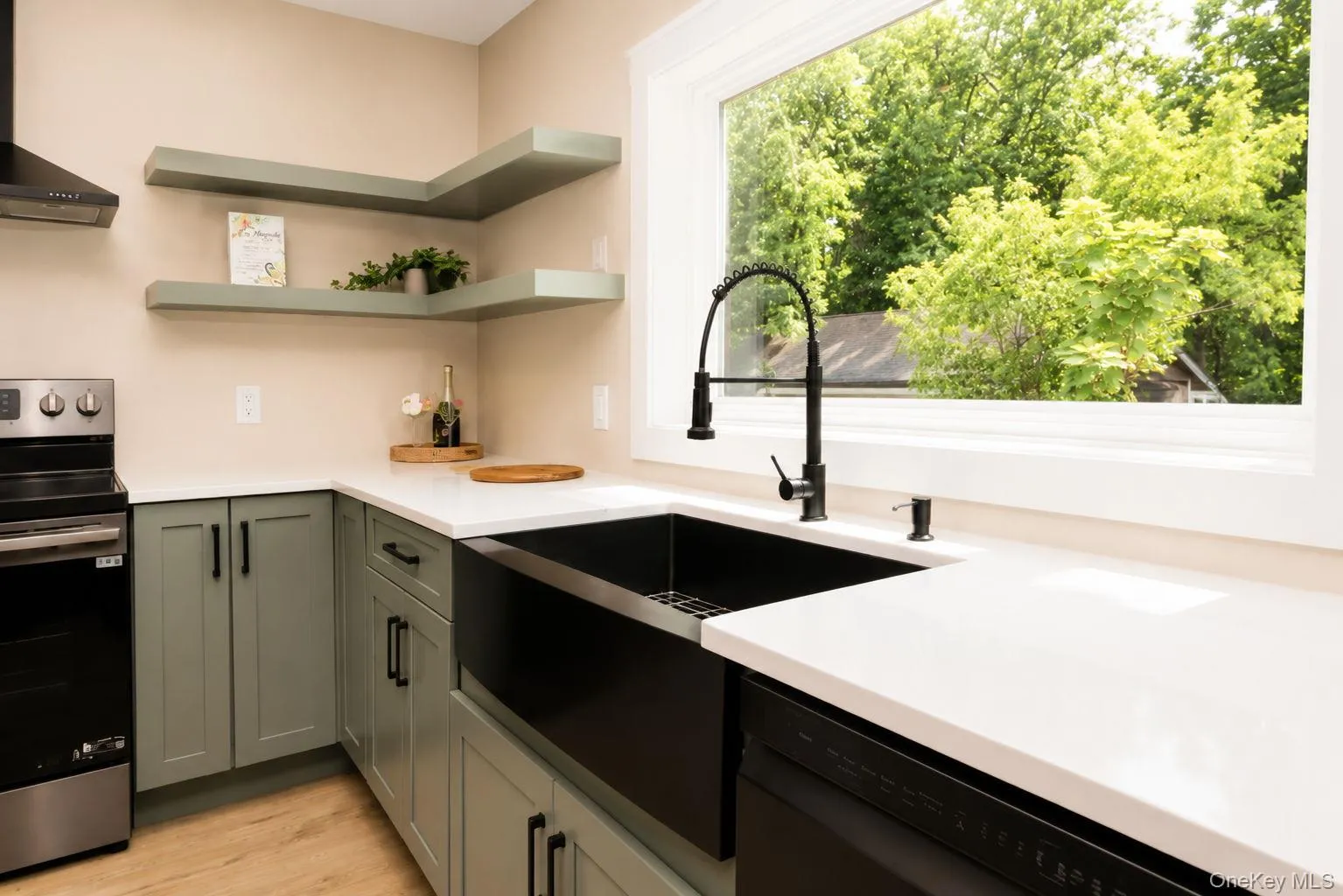 Kitchen featuring sage green cabinetry, white countertops, a black farmhouse sink with a matte black faucet, and wood-finish flooring Kitchen featuring sage green cabinetry, white countertops, a black farmhouse sink with a matte black faucet, and wood-finish flooring