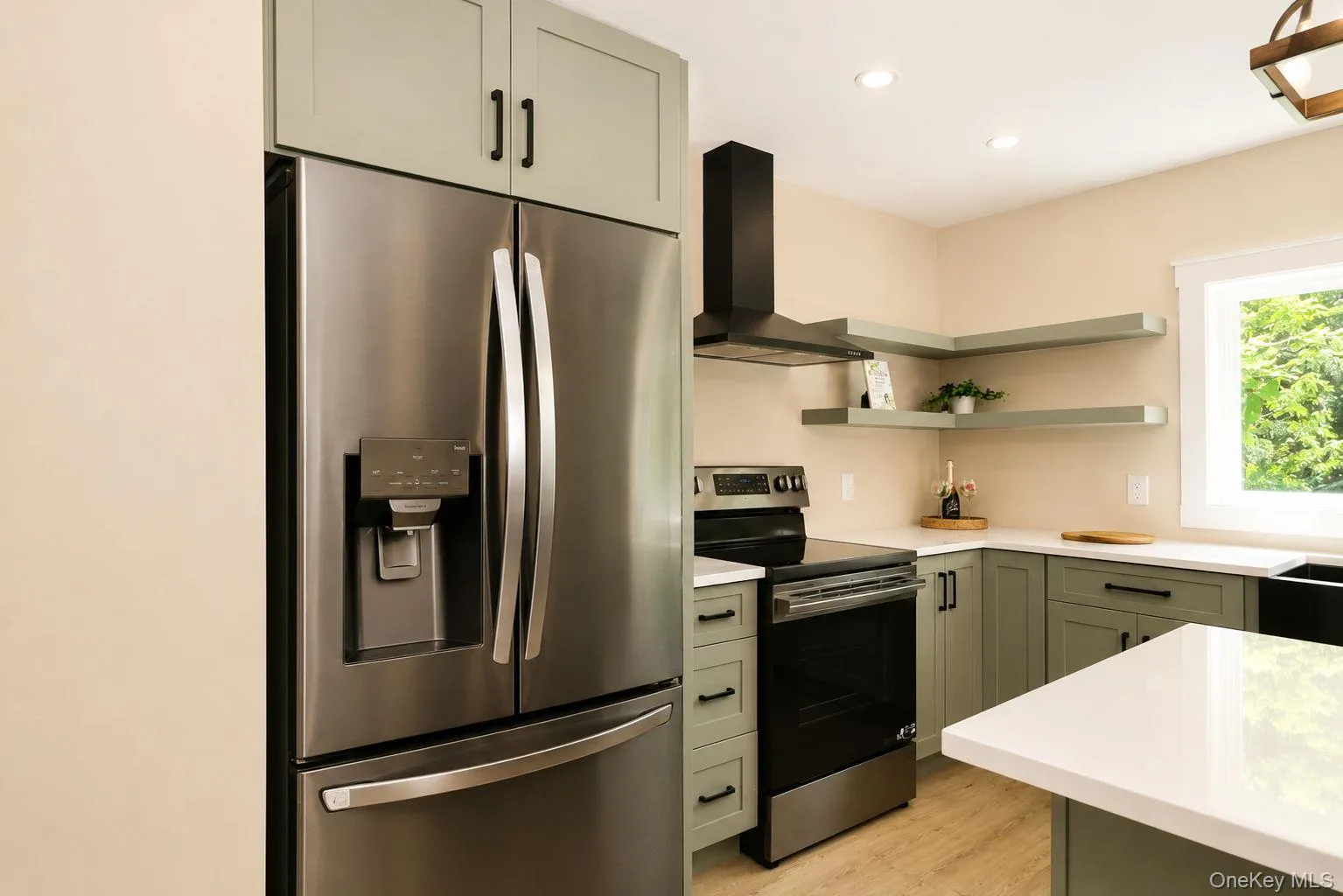 Modern kitchen featuring stainless steel appliances, sage green cabinetry with matte black hardware, white countertops, and open shelving Modern kitchen featuring stainless steel appliances, sage green cabinetry with matte black hardware, white countertops, and open shelving