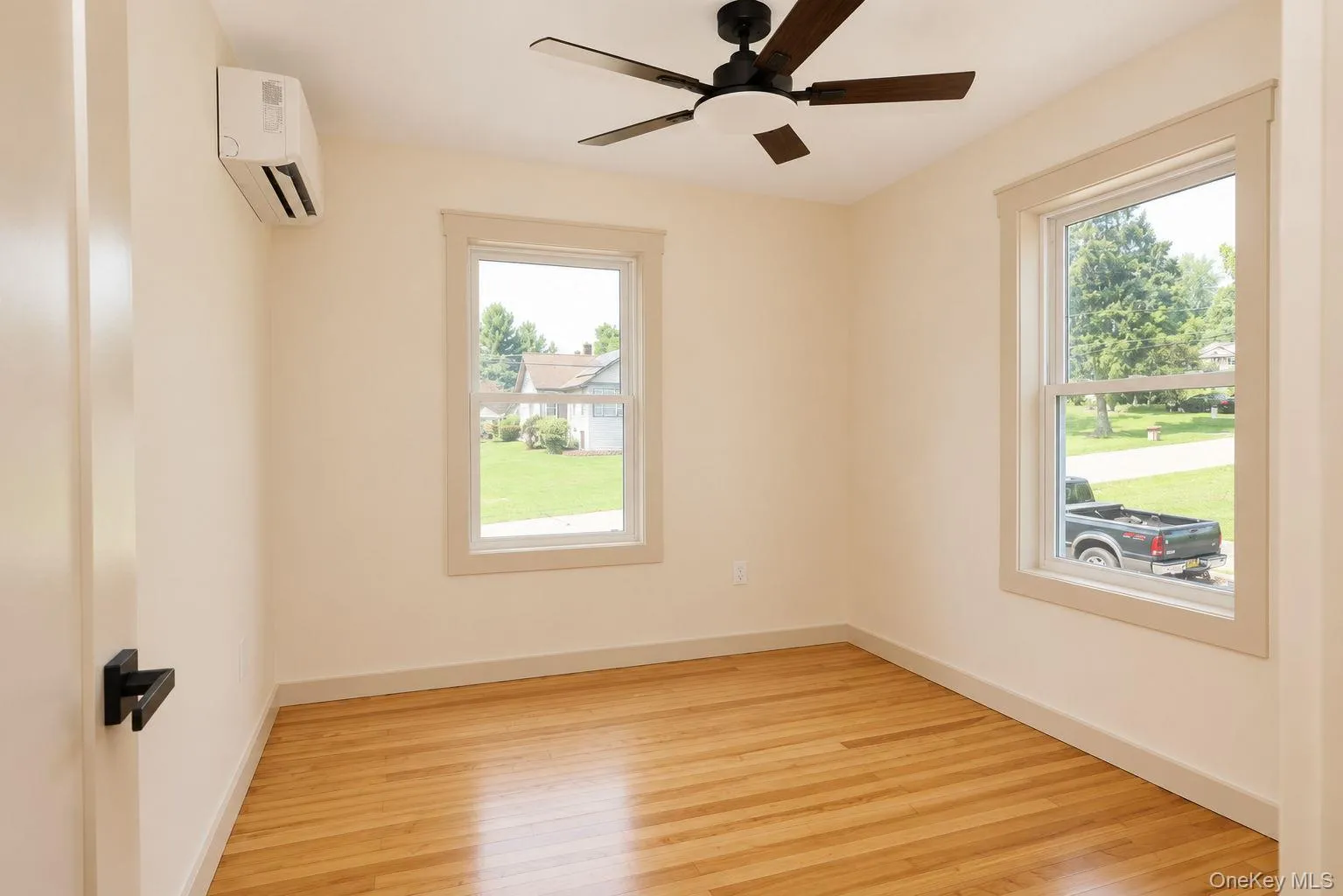 Bright interior room featuring wood-finish flooring, a ceiling fan with integrated lighting, and two windows with white trim Bright interior room featuring wood-finish flooring, a ceiling fan with integrated lighting, and two windows with white trim