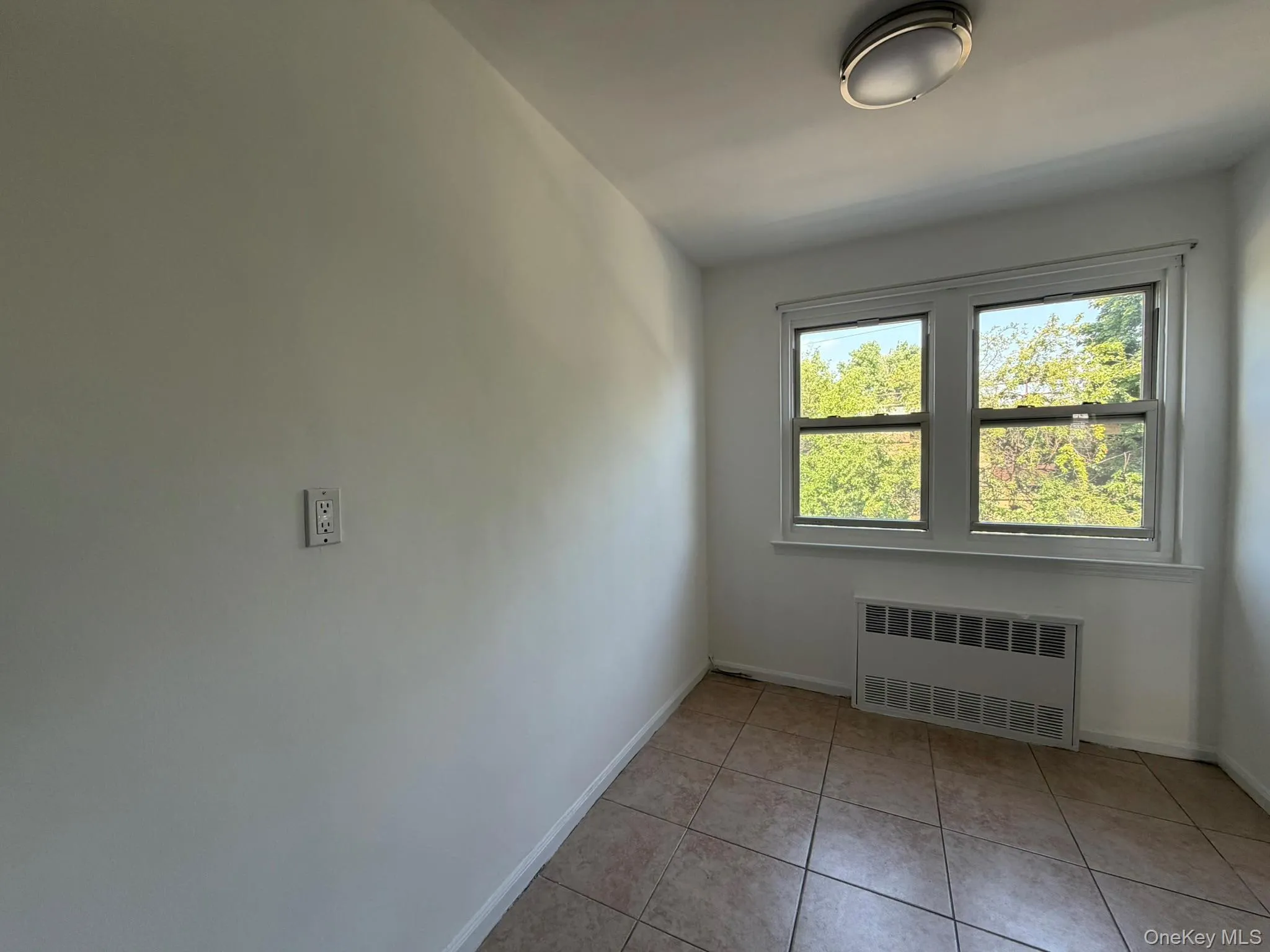 Room featuring two windows, neutral wall tones, tile flooring, baseboard trim, and a ceiling-mounted light fixture Room featuring two windows, neutral wall tones, tile flooring, baseboard trim, and a ceiling-mounted light fixture