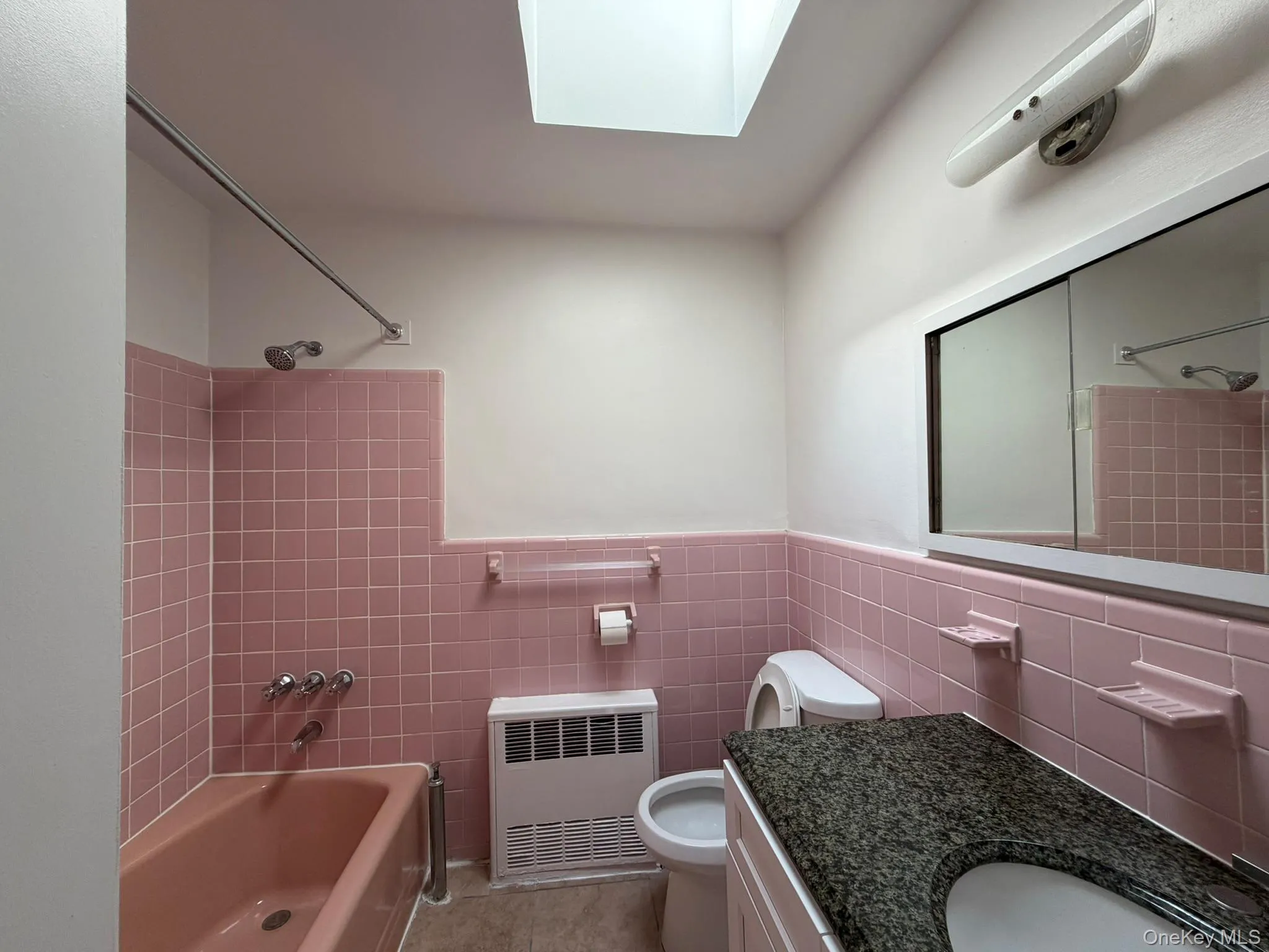 Bathroom featuring a skylight, pink subway tile walls, and a granite-finish countertop with an integrated sink Bathroom featuring a skylight, pink subway tile walls, and a granite-finish countertop with an integrated sink