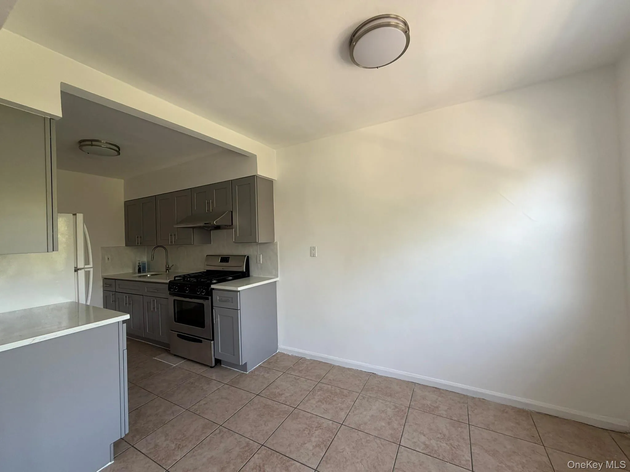 Open kitchen area featuring grey shaker-style cabinetry, light-toned countertops, and a stainless steel oven/range Open kitchen area featuring grey shaker-style cabinetry, light-toned countertops, and a stainless steel oven/range