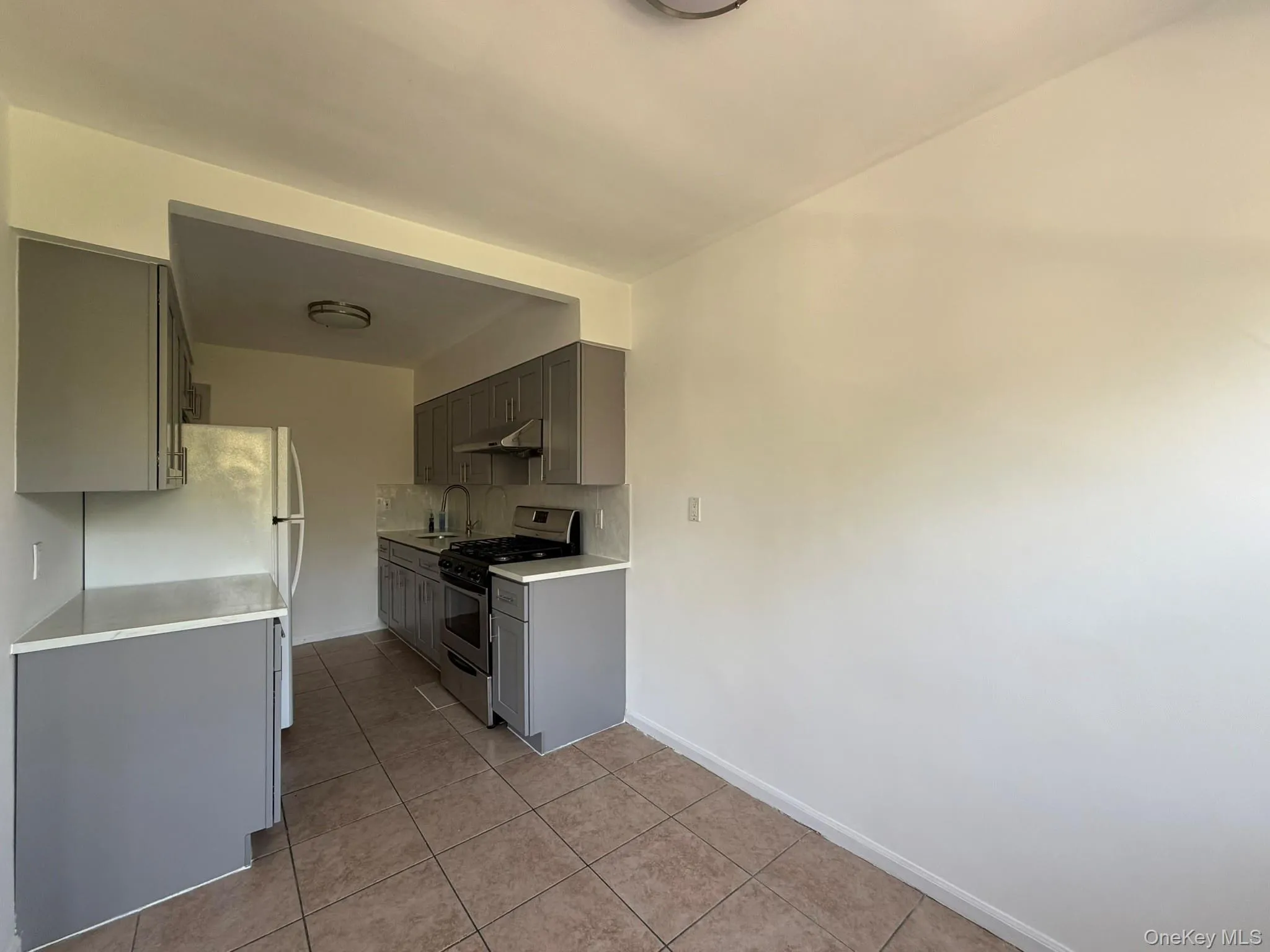 Kitchen featuring gray cabinetry, white countertops, tile flooring, a stainless steel range, and a stainless steel refrigerator Kitchen featuring gray cabinetry, white countertops, tile flooring, a stainless steel range, and a stainless steel refrigerator