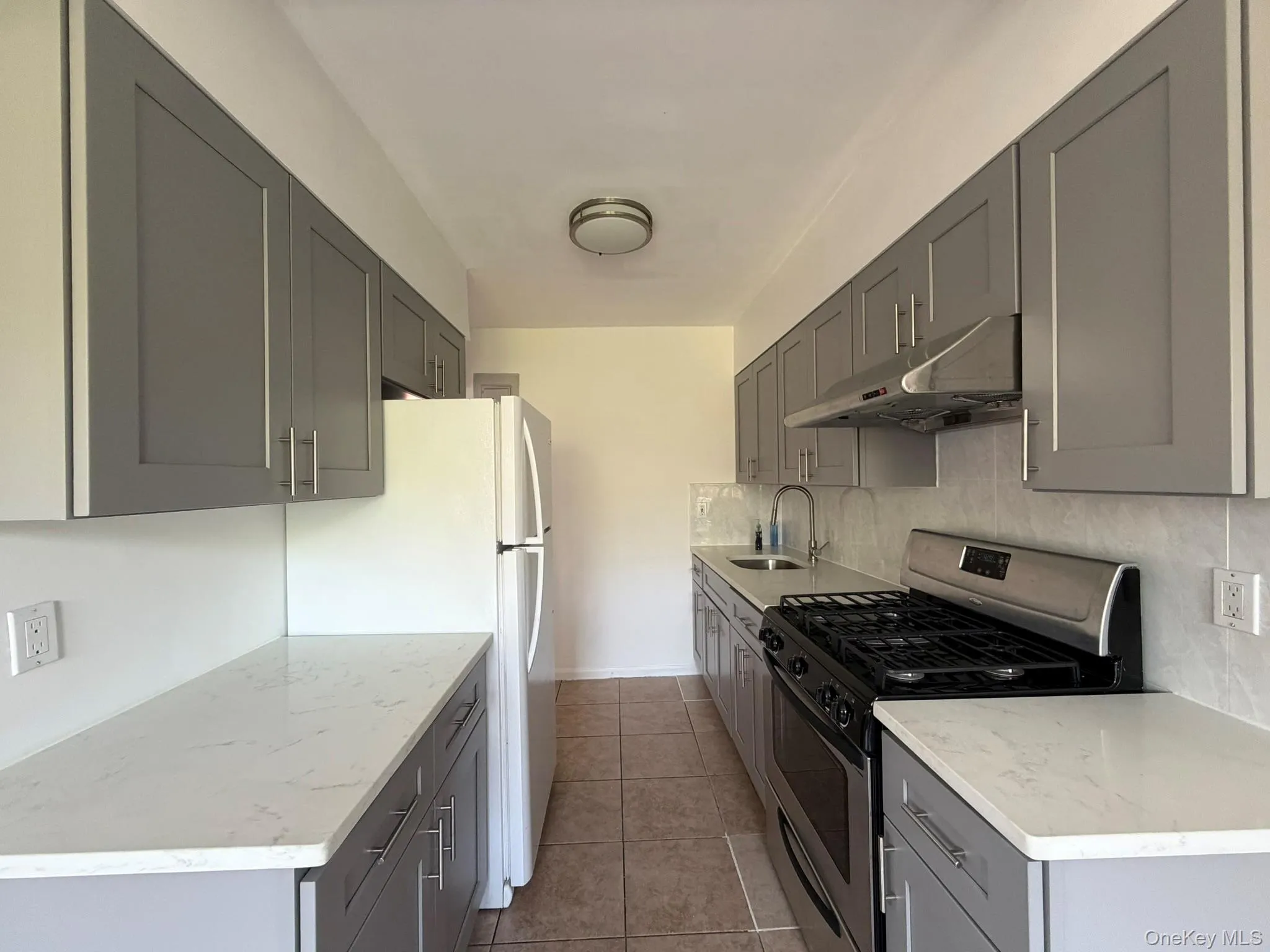 Galley kitchen featuring gray shaker-style cabinetry, white quartz countertops, stainless steel appliances, and a tiled backsplash Galley kitchen featuring gray shaker-style cabinetry, white quartz countertops, stainless steel appliances, and a tiled backsplash