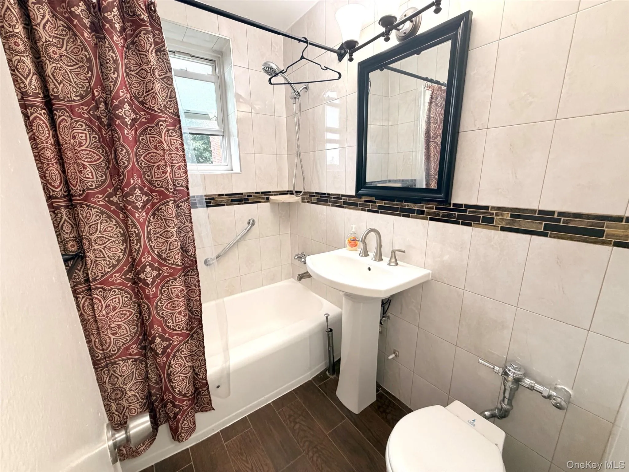 Full bathroom featuring a pedestal sink, a rectangular framed mirror with overhead lighting, and a combination tub and shower Full bathroom featuring a pedestal sink, a rectangular framed mirror with overhead lighting, and a combination tub and shower
