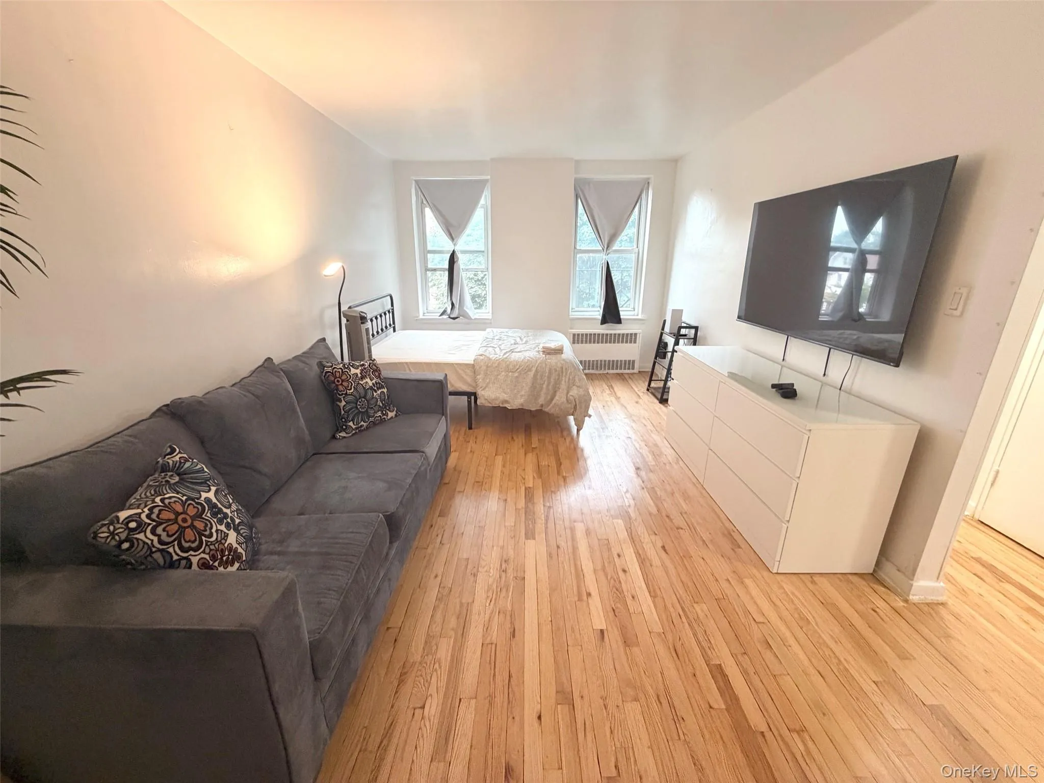 Open-concept living area featuring wood-finish flooring, white walls, and two large windows Open-concept living area featuring wood-finish flooring, white walls, and two large windows