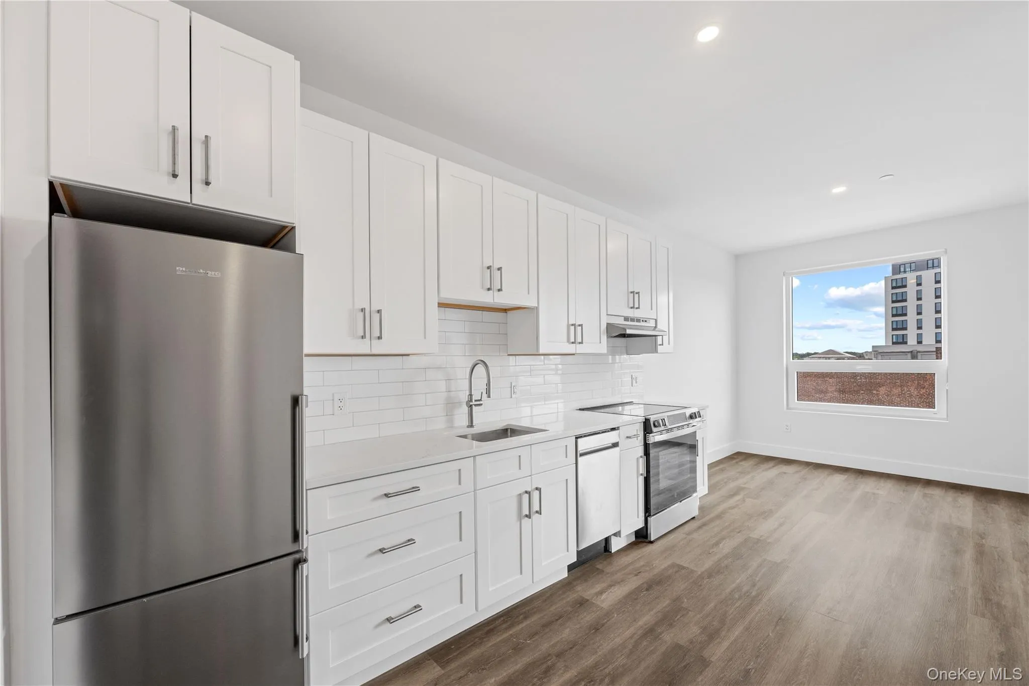 Modern kitchen featuring white shaker cabinetry, stainless steel appliances, white subway tile backsplash, and wood-finish flooring Modern kitchen featuring white shaker cabinetry, stainless steel appliances, white subway tile backsplash, and wood-finish flooring