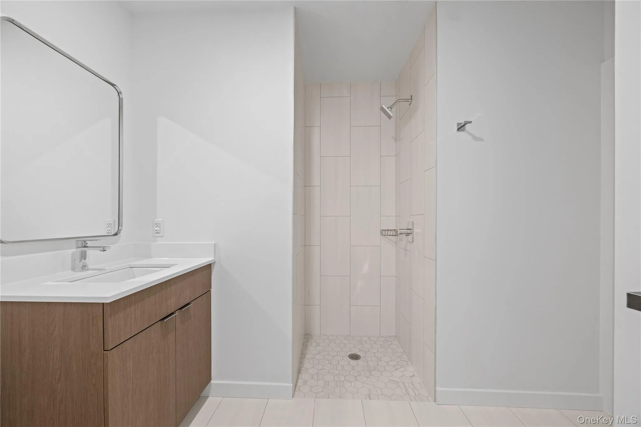 Contemporary bathroom featuring a wood-finish vanity with an integrated sink, a rectangular mirror, a walk-in shower with vertical tile detailing, and a pebble-tiled shower floor Contemporary bathroom featuring a wood-finish vanity with an integrated sink, a rectangular mirror, a walk-in shower with vertical tile detailing, and a pebble-tiled shower floor