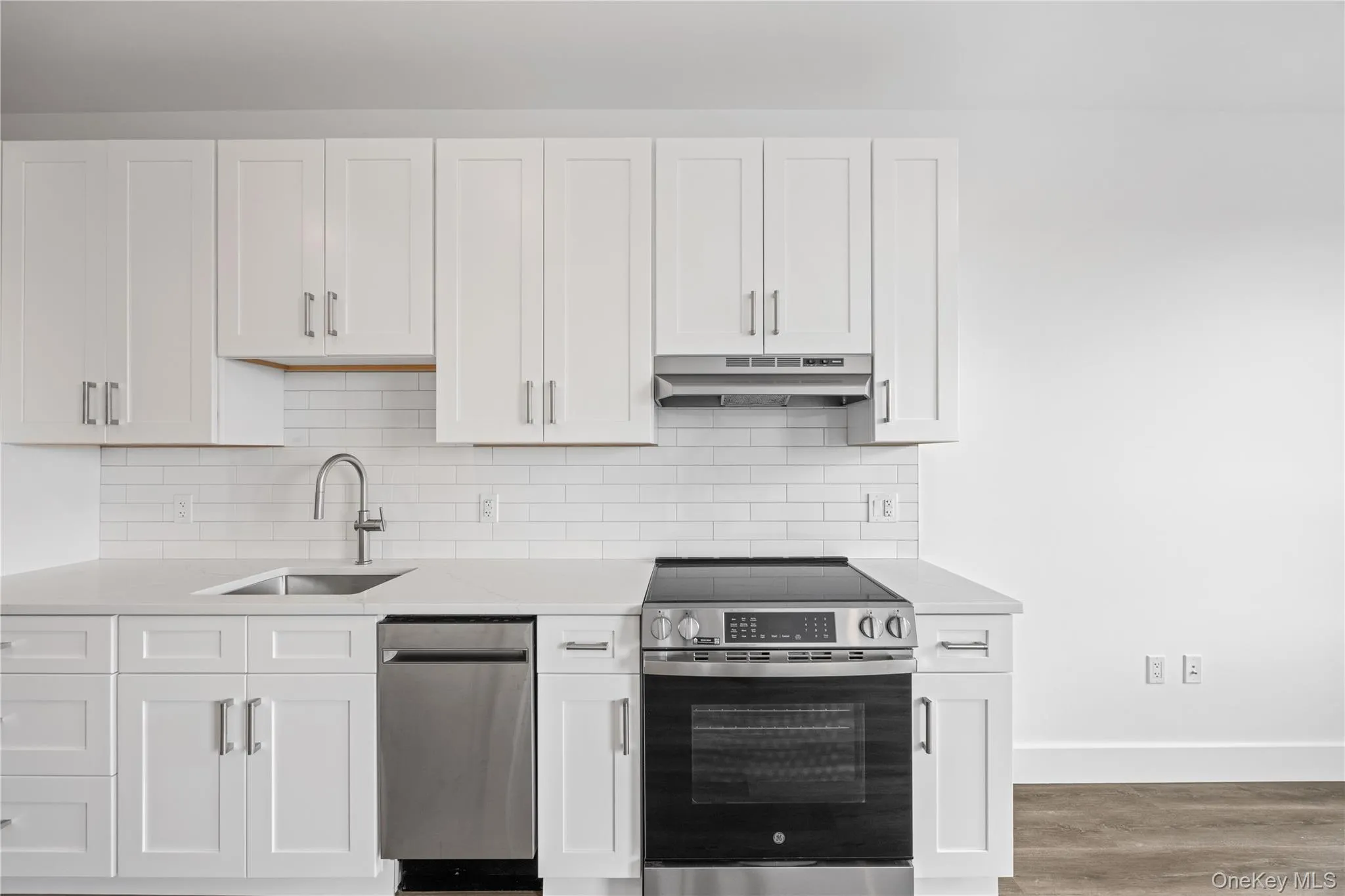 Modern kitchen featuring white shaker cabinetry, stainless steel appliances, a subway tile backsplash, and light-toned countertops Modern kitchen featuring white shaker cabinetry, stainless steel appliances, a subway tile backsplash, and light-toned countertops
