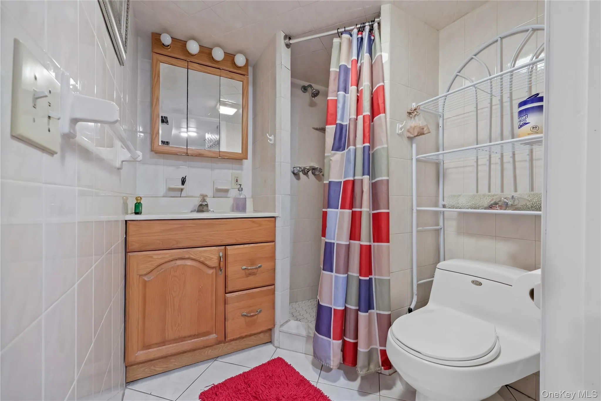 Bathroom with tile walls, light tile patterned floors, vanity, and a stall shower Bathroom with tile walls, light tile patterned floors, vanity, and a stall shower