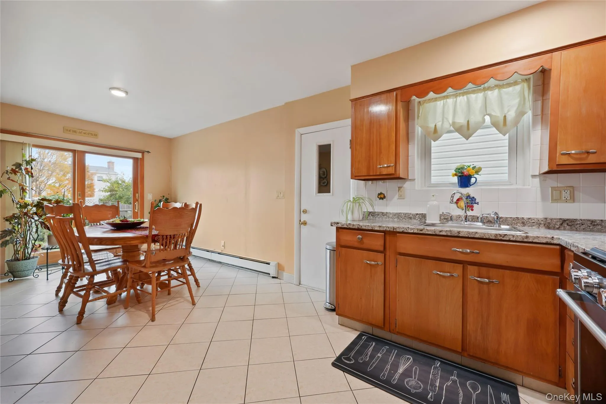 Kitchen with brown cabinets, stainless steel range with gas stovetop, a baseboard heating unit, and light tile patterned flooring Kitchen with brown cabinets, stainless steel range with gas stovetop, a baseboard heating unit, and light tile patterned flooring