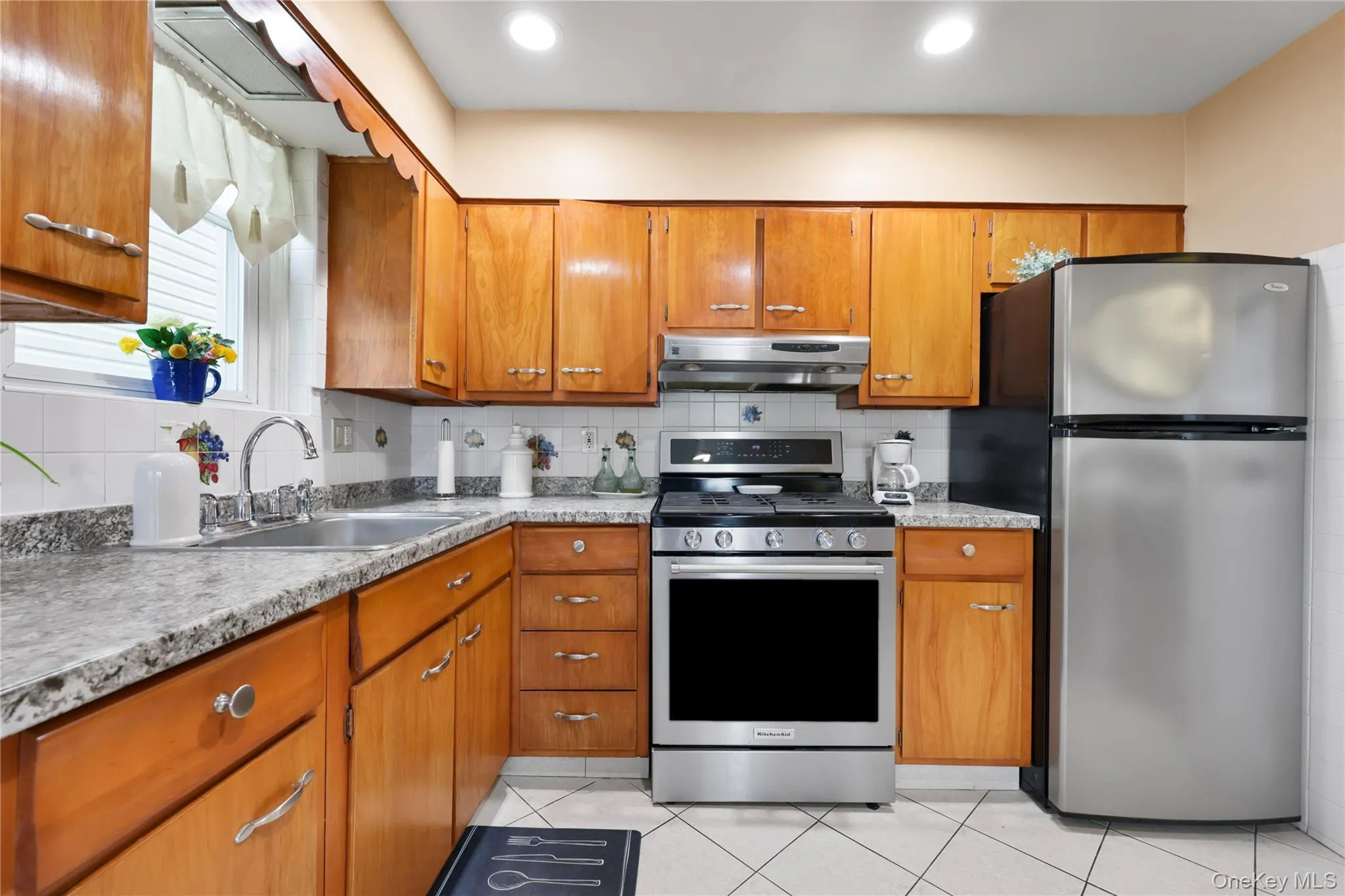 Kitchen with backsplash, appliances with stainless steel finishes, brown cabinetry, and light tile patterned flooring Kitchen with backsplash, appliances with stainless steel finishes, brown cabinetry, and light tile patterned flooring