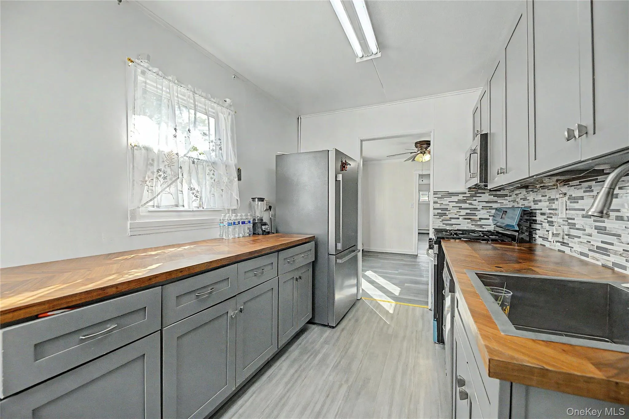 Kitchen featuring light gray cabinetry, stainless steel appliances, wood-finish countertops, and a textured tile backsplash Kitchen featuring light gray cabinetry, stainless steel appliances, wood-finish countertops, and a textured tile backsplash