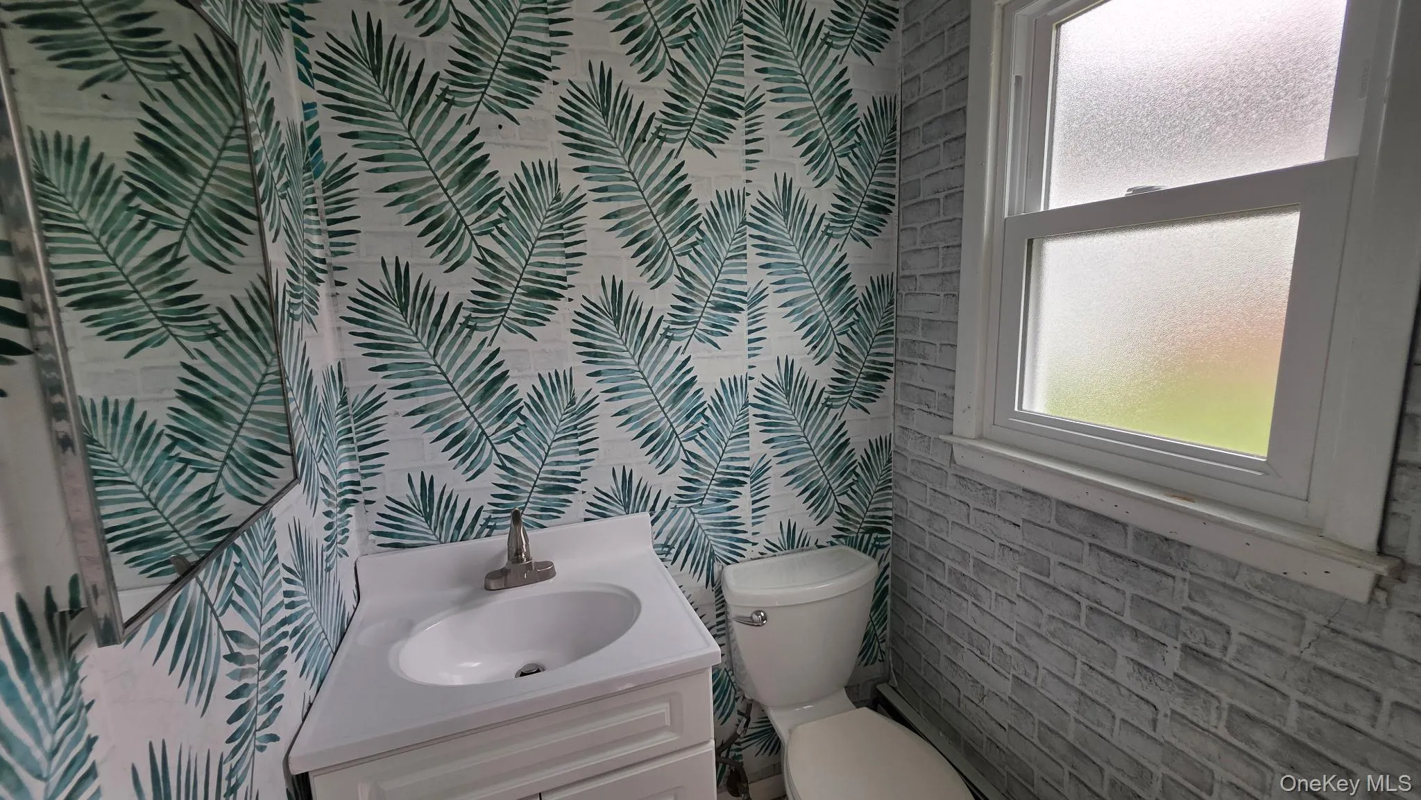 Powder room featuring a white single-sink vanity with a chrome faucet, a wall-mounted mirror, a standard toilet, and a frosted window Powder room featuring a white single-sink vanity with a chrome faucet, a wall-mounted mirror, a standard toilet, and a frosted window