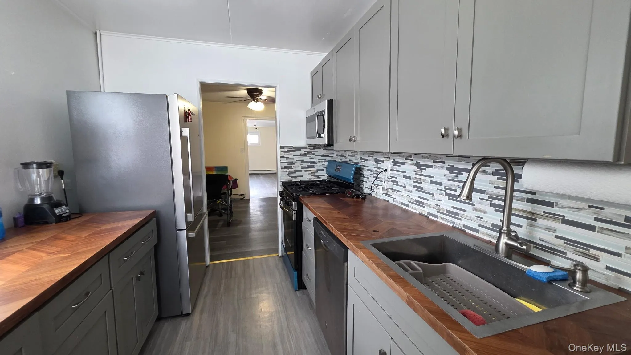 Galley kitchen featuring gray cabinetry, wood-finish countertops, stainless steel appliances, and a mosaic tile backsplash Galley kitchen featuring gray cabinetry, wood-finish countertops, stainless steel appliances, and a mosaic tile backsplash