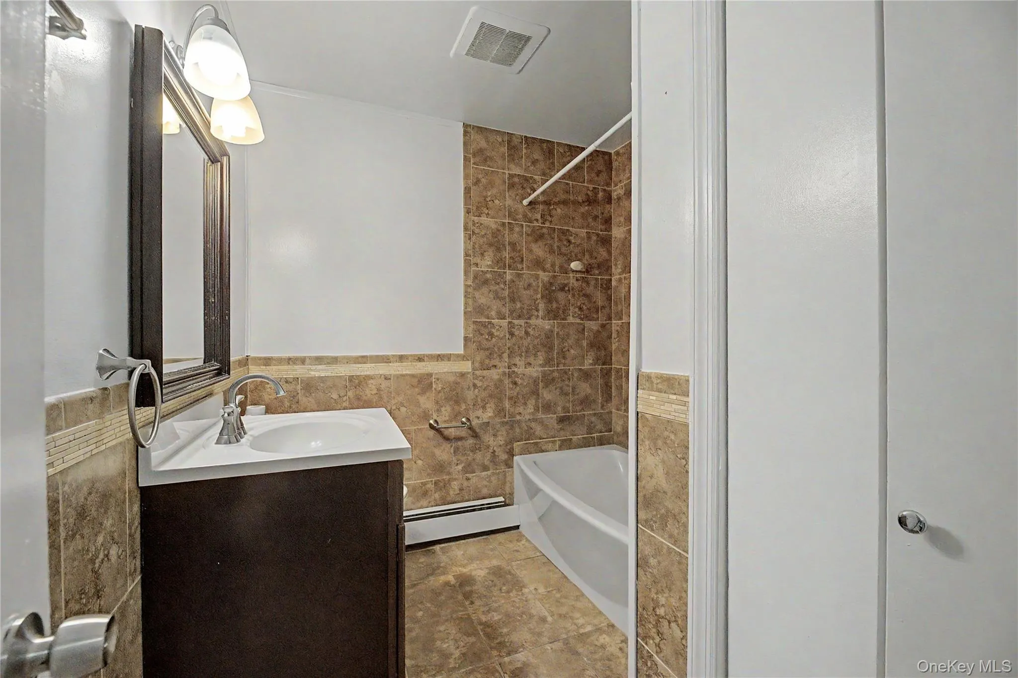 Vanity with a white countertop and integrated sink, mirrored medicine cabinet, wall-mounted light fixture, tile flooring, and a tiled shower/tub combination Vanity with a white countertop and integrated sink, mirrored medicine cabinet, wall-mounted light fixture, tile flooring, and a tiled shower/tub combination