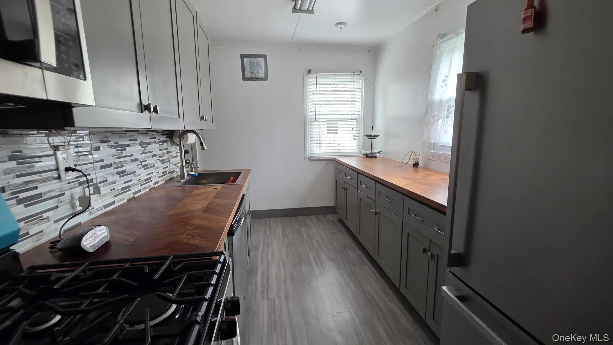 Kitchen featuring wood-finish countertops, grey cabinetry, a mosaic tile backsplash, and stainless steel appliances Kitchen featuring wood-finish countertops, grey cabinetry, a mosaic tile backsplash, and stainless steel appliances
