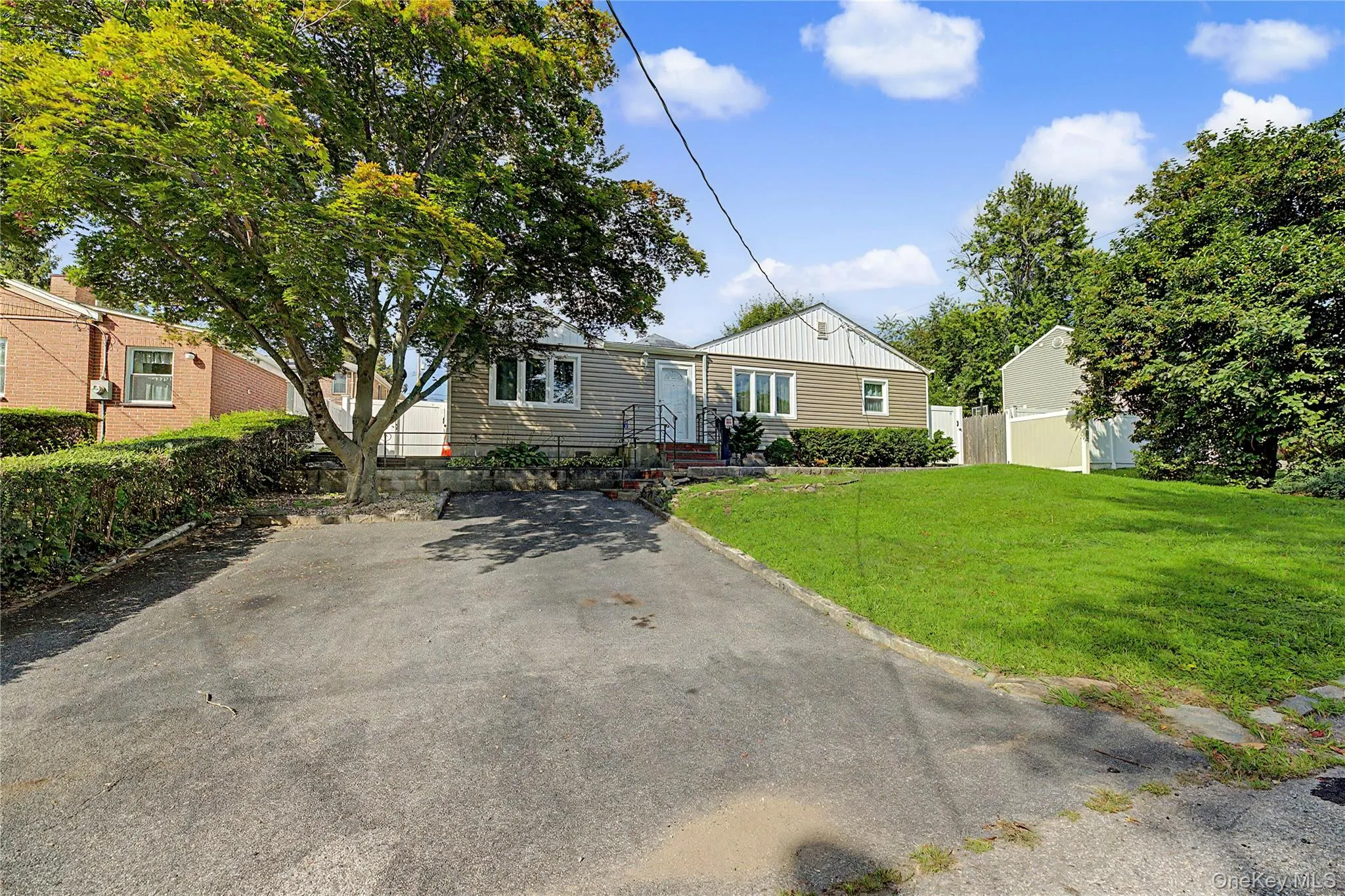 Ranch-style residence featuring a sloped asphalt driveway, mature front yard tree, and manicured lawn Ranch-style residence featuring a sloped asphalt driveway, mature front yard tree, and manicured lawn