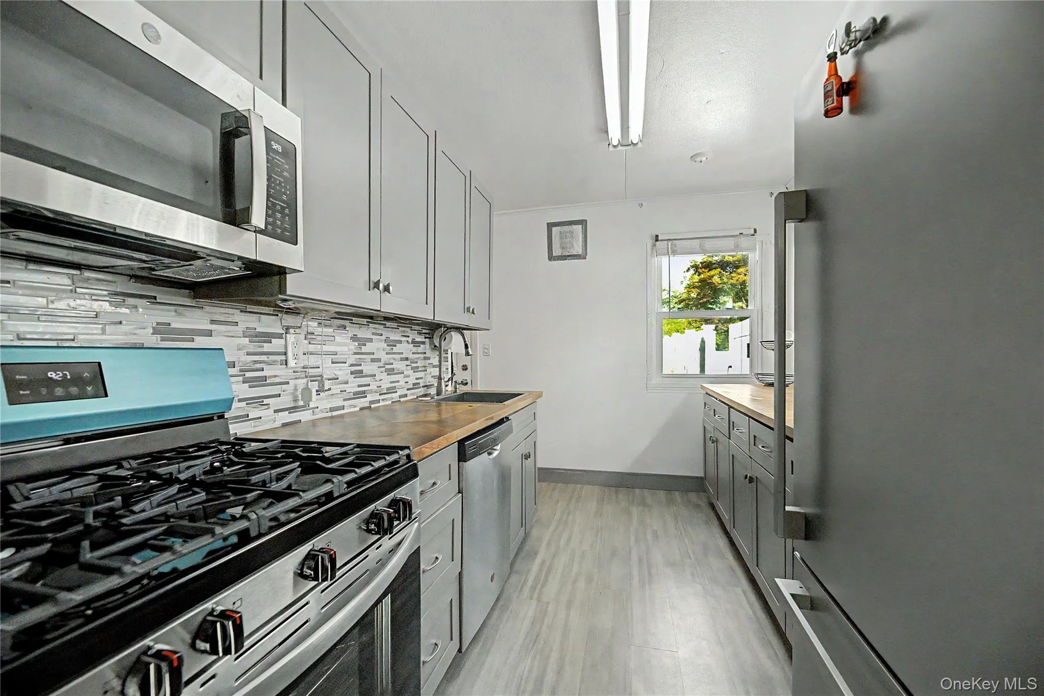 Kitchen featuring light gray cabinetry, stainless steel appliances, wood-finish countertops, and a textured tile backsplash Kitchen featuring light gray cabinetry, stainless steel appliances, wood-finish countertops, and a textured tile backsplash