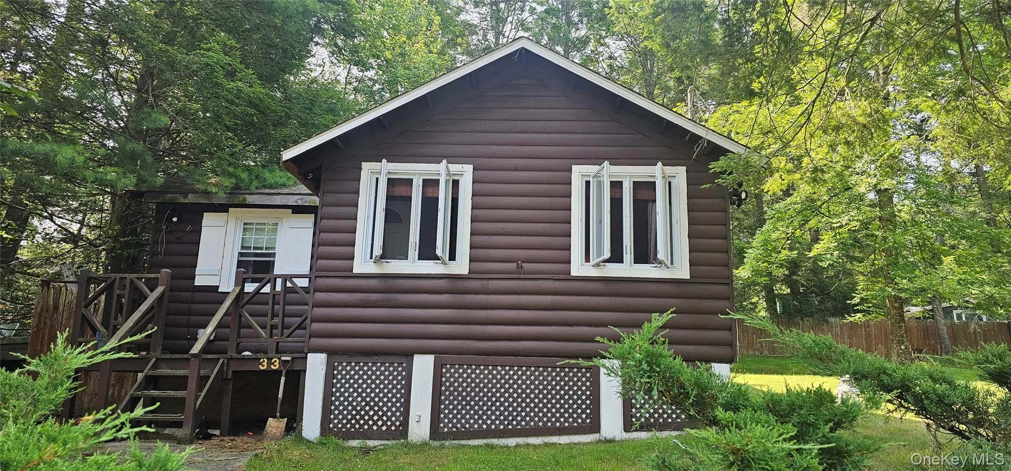 Brown log-style siding exterior with white window frames and open casement windows Brown log-style siding exterior with white window frames and open casement windows