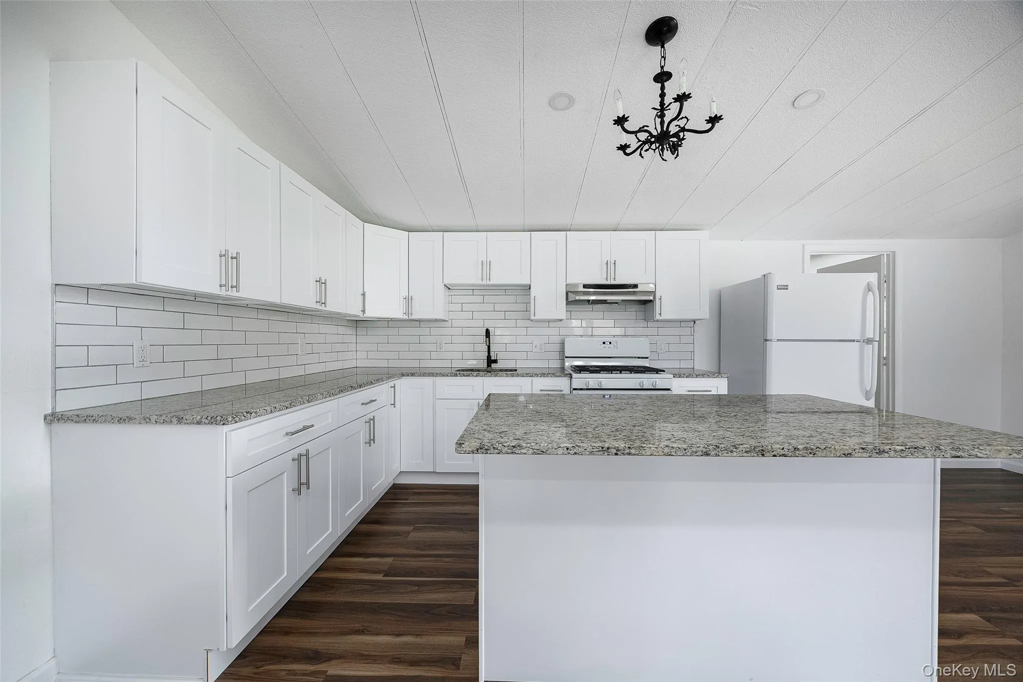 Kitchen with a center island, white appliances, dark wood finished floors, and white cabinetry Kitchen with a center island, white appliances, dark wood finished floors, and white cabinetry
