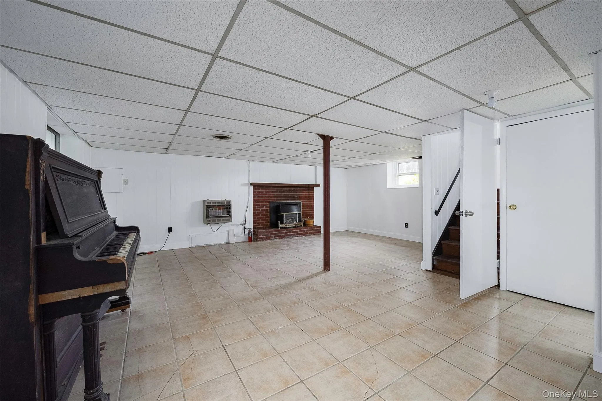 Basement featuring a paneled ceiling, stairs, light tile patterned floors, heating unit, and a fireplace Basement featuring a paneled ceiling, stairs, light tile patterned floors, heating unit, and a fireplace