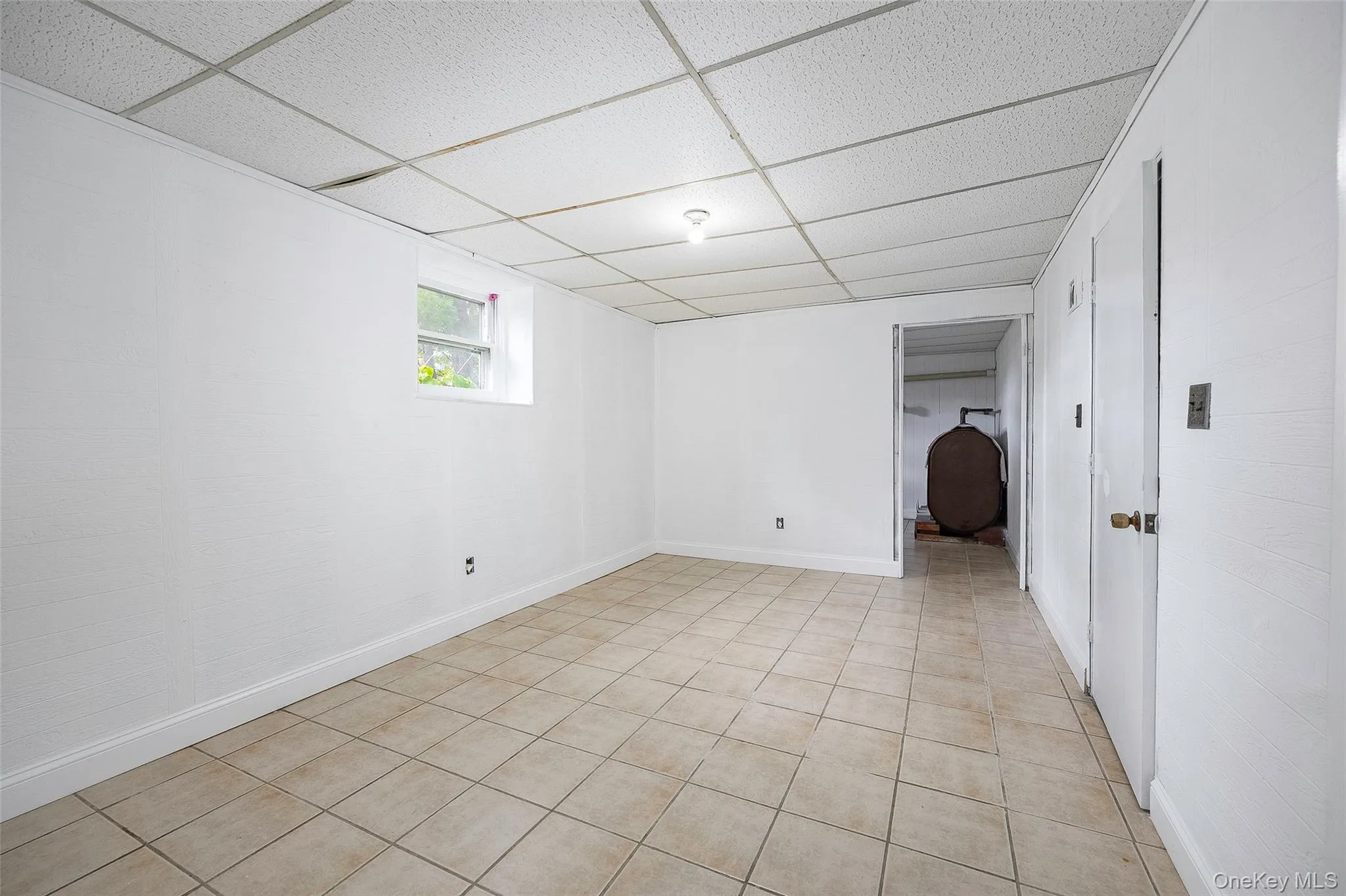 Below grade area with a paneled ceiling, heating fuel, and light tile patterned floors Below grade area with a paneled ceiling, heating fuel, and light tile patterned floors