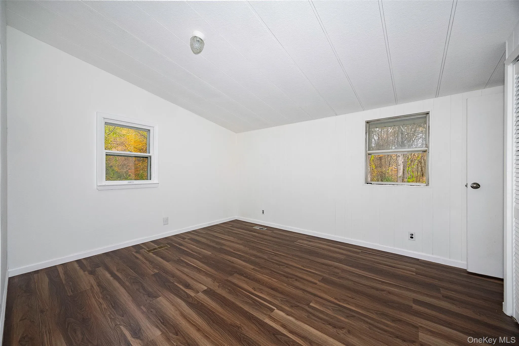 Unfurnished room with dark wood finished floors and vaulted ceiling Unfurnished room with dark wood finished floors and vaulted ceiling