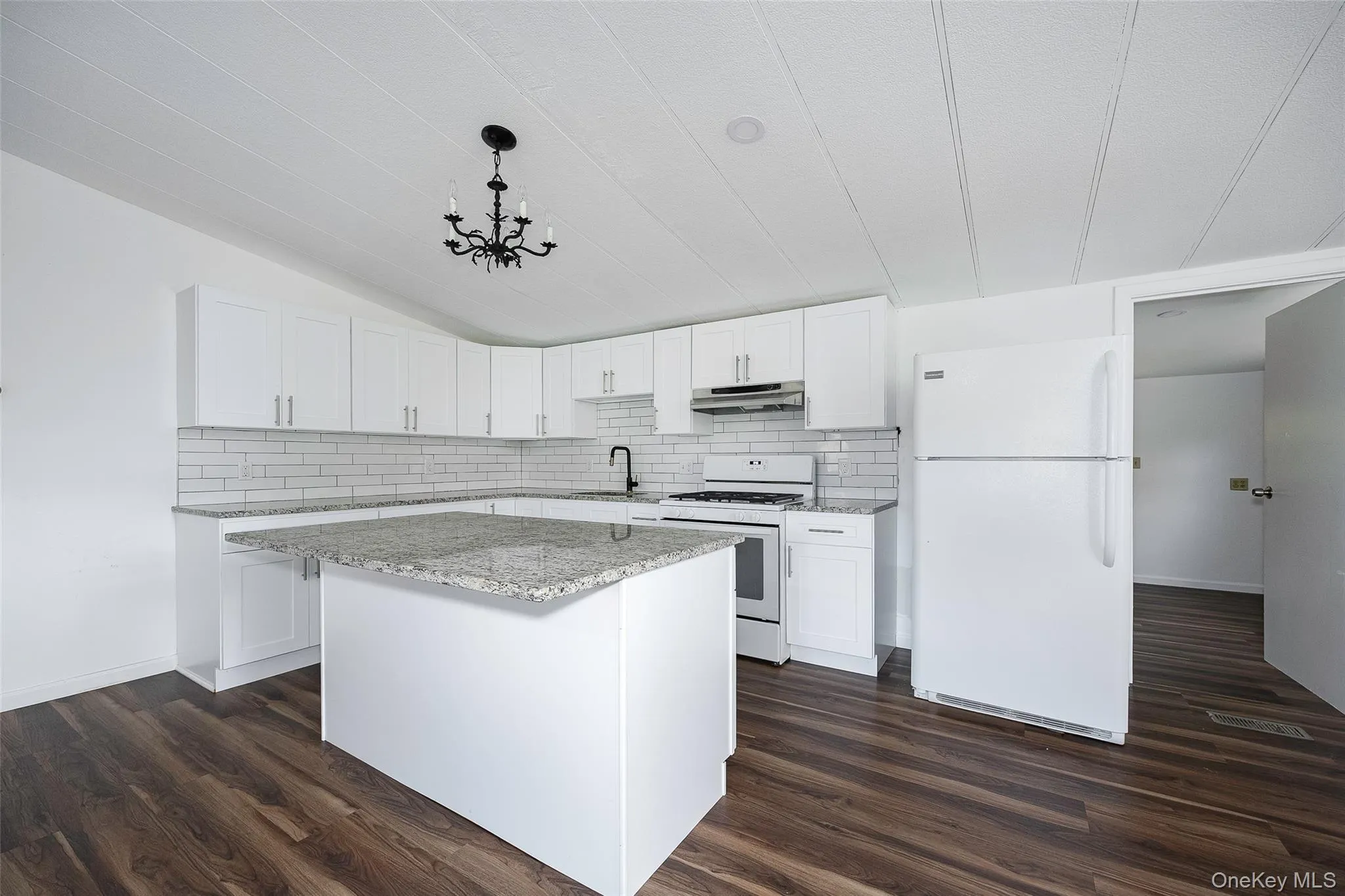 Kitchen featuring white appliances, white cabinetry, backsplash, light stone counters, and vaulted ceiling Kitchen featuring white appliances, white cabinetry, backsplash, light stone counters, and vaulted ceiling