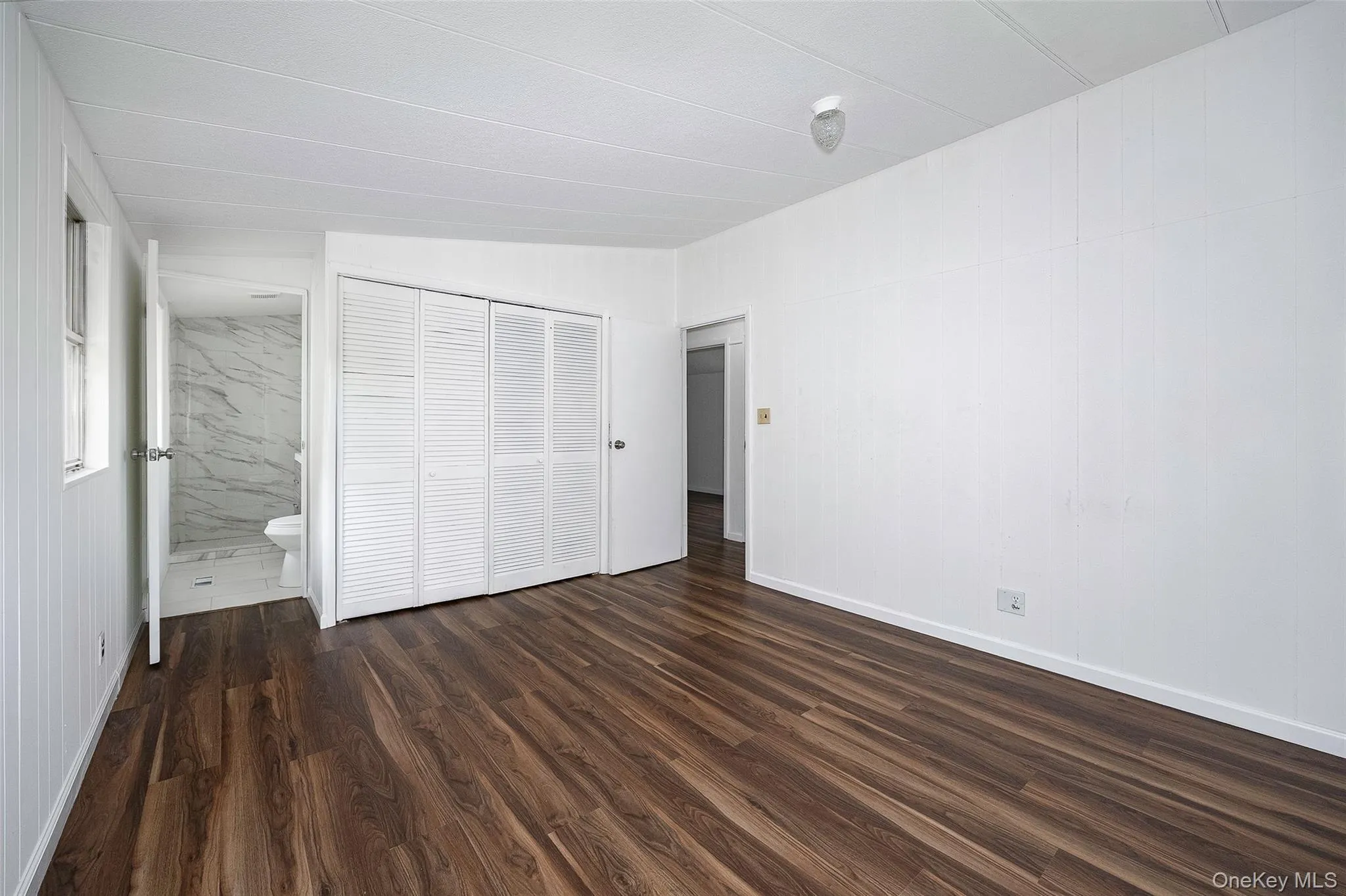 Unfurnished bedroom with dark wood-type flooring, a closet, and ensuite bath Unfurnished bedroom with dark wood-type flooring, a closet, and ensuite bath